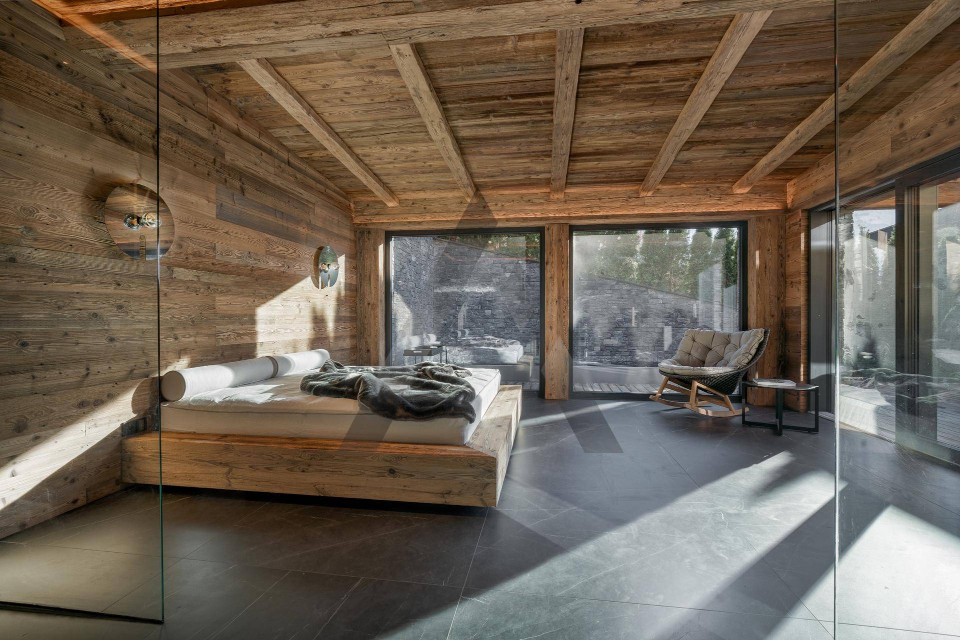 Entspannungsbereich mit Holzwänden, großzügigen Fenstern und einem Liegebett, ideal zum Verweilen.