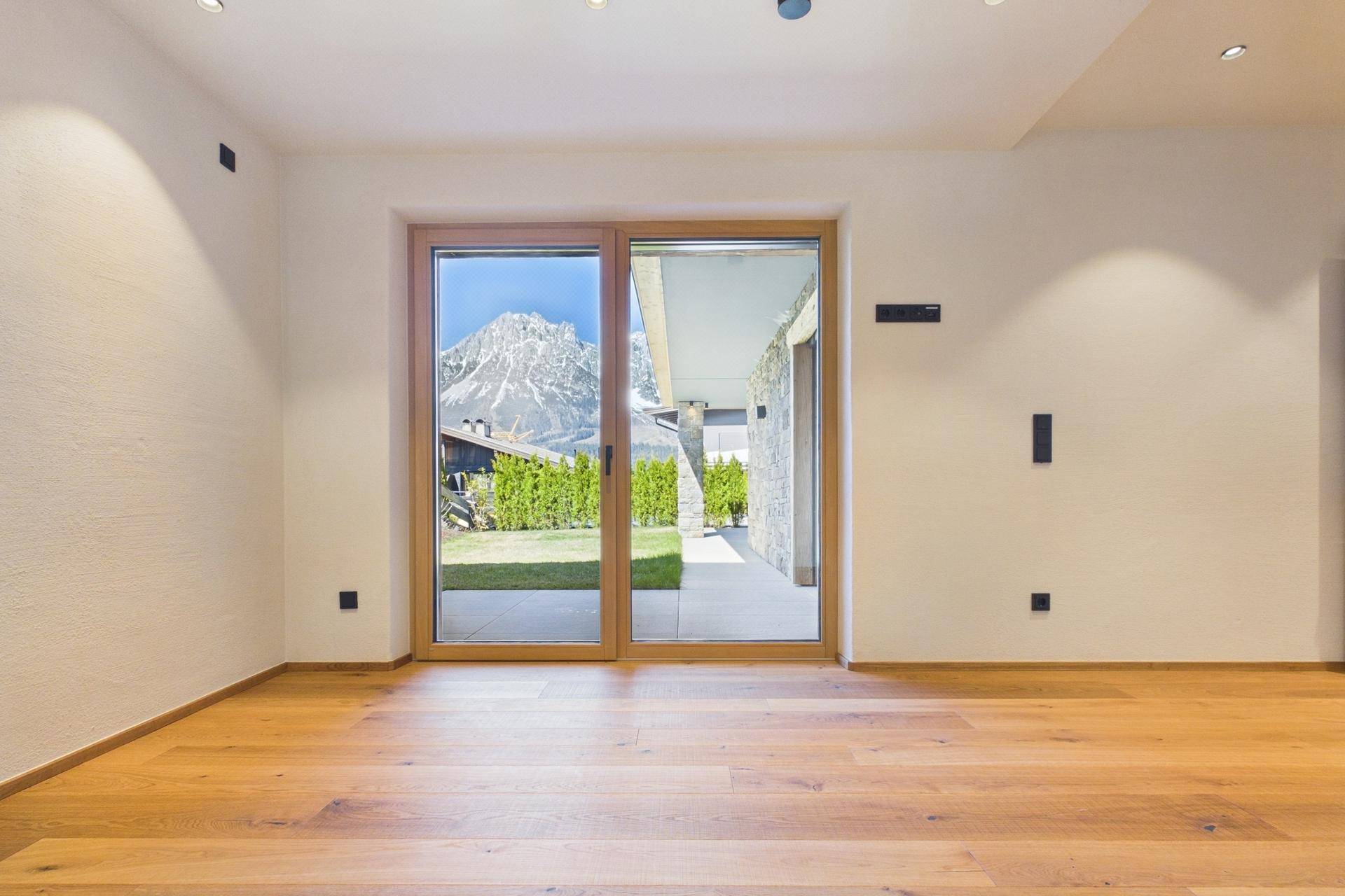 Heller Raum mit Holzboden und Schiebetür zur Terrasse mit Bergblick.