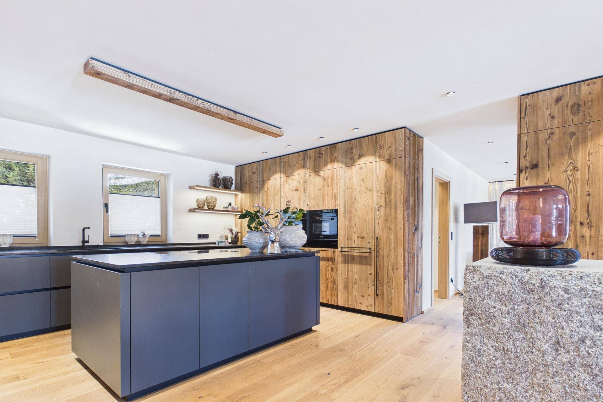 Moderne Küche mit Holzfronten, dunkler Kücheninsel und Holzboden, offen gestaltet und hell.