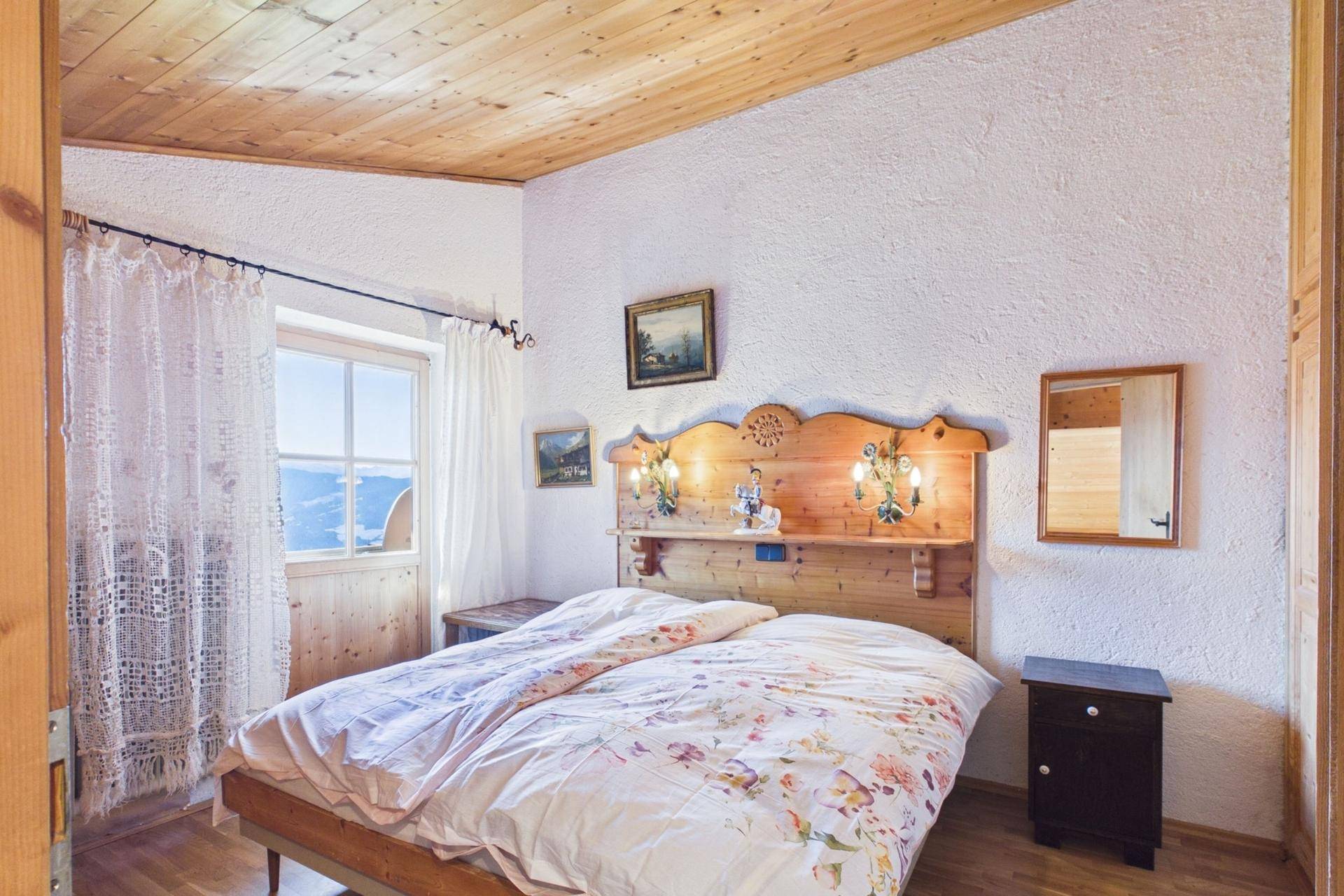 Schlafzimmer im Landhausstil mit Holzbett, Holzbalkendecke und Bergblick.