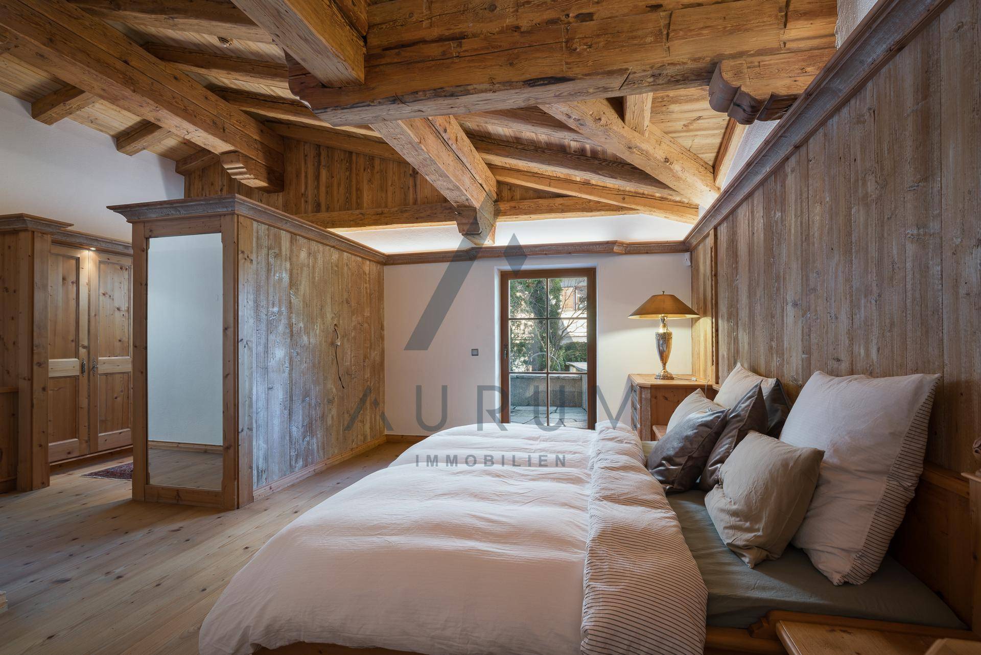 Helles Schlafzimmer mit Holzwänden, Holzbalkendecke und Zugang zum Außenbereich.