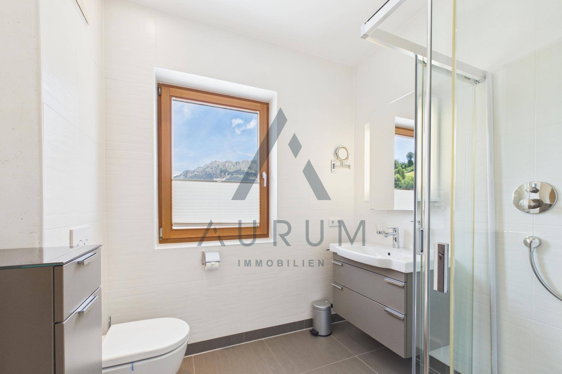 Helles Badezimmer mit Dusche, modernem Waschtisch und Fenster mit Bergblick.
