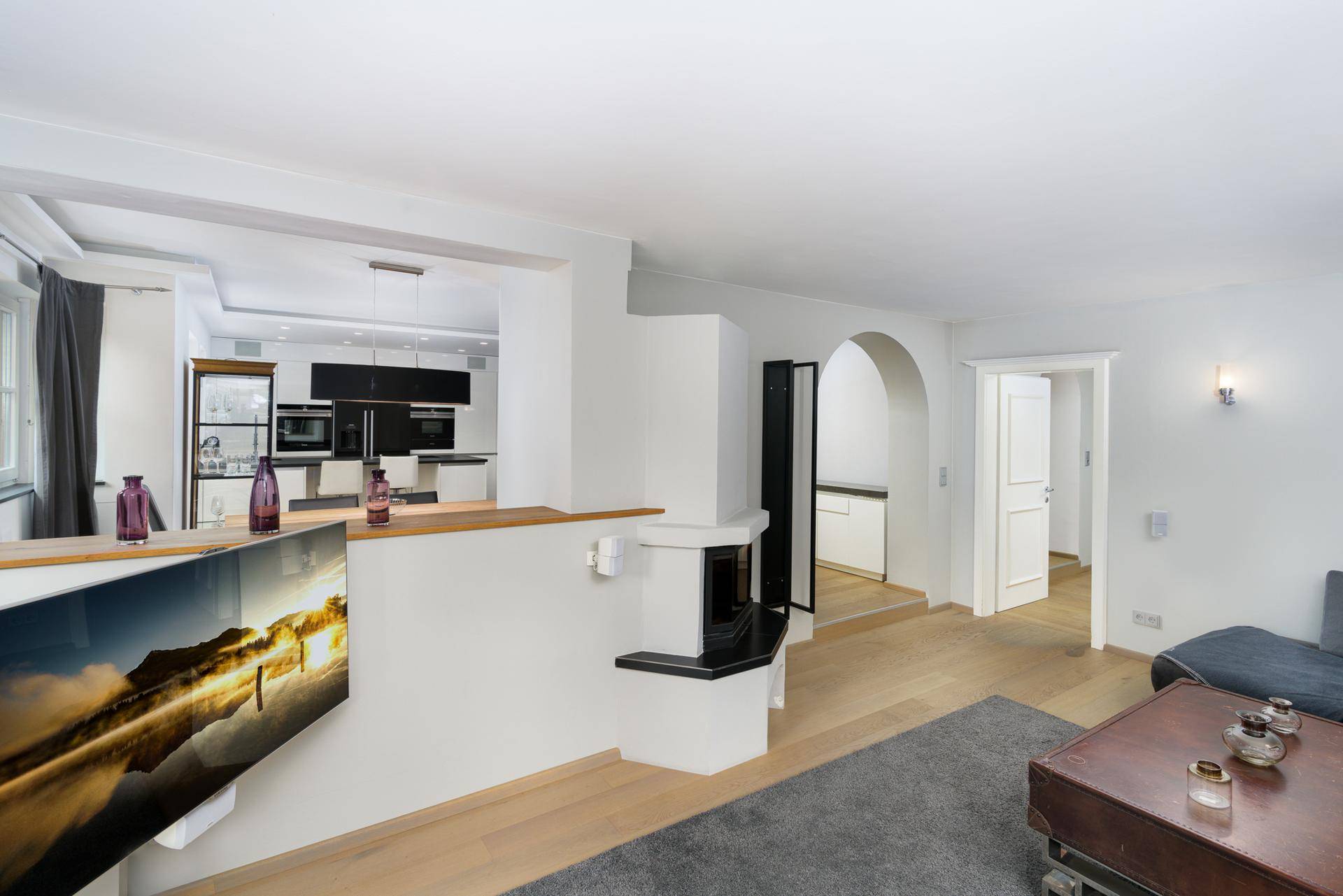 Offener Wohnbereich mit Kamin, Blick auf die moderne Küche und Zugang zu weiteren Räumen.