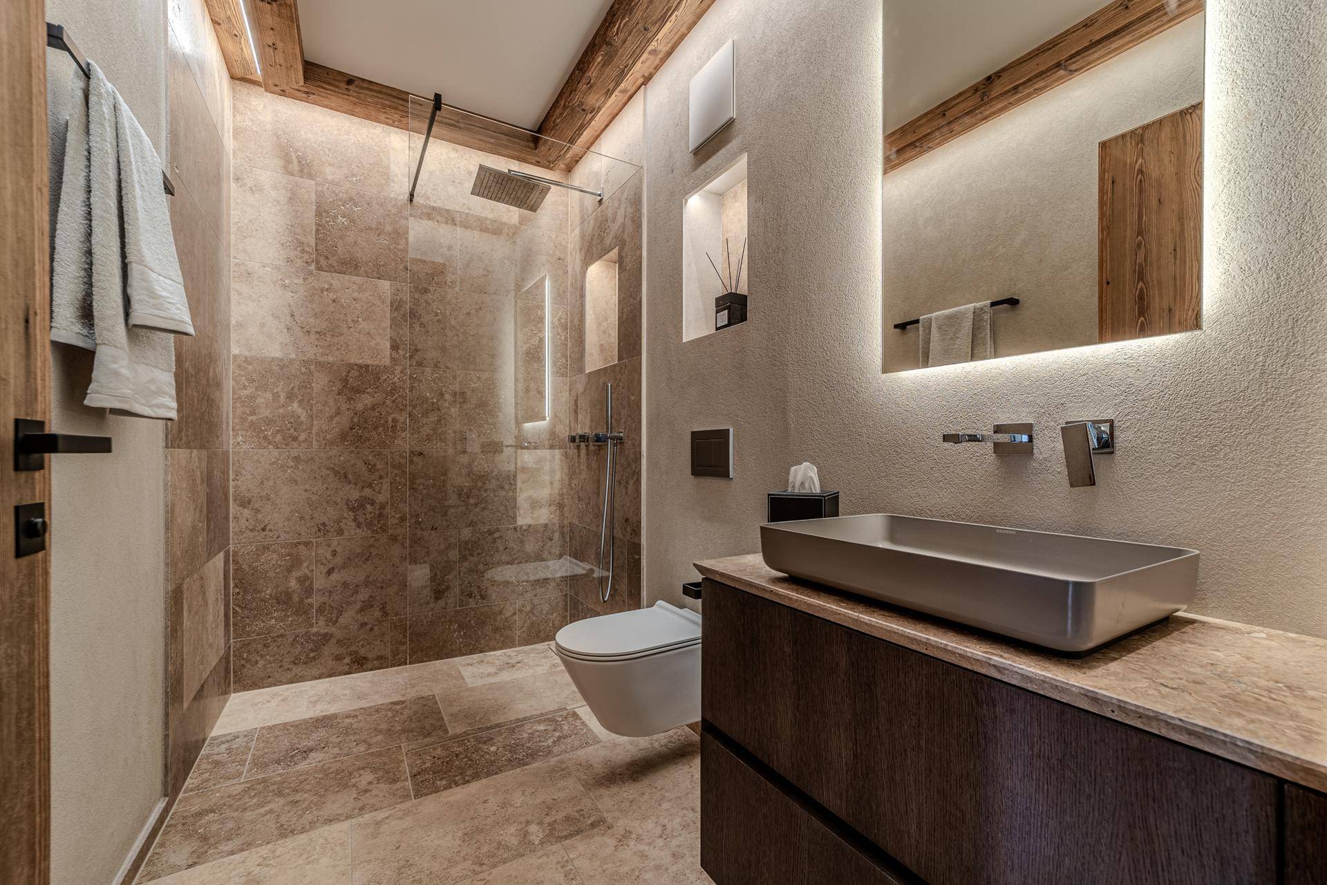Modernes Badezimmer mit begehbarer Dusche, Wand-WC und stilvollem Waschtisch mit Beleuchtung.