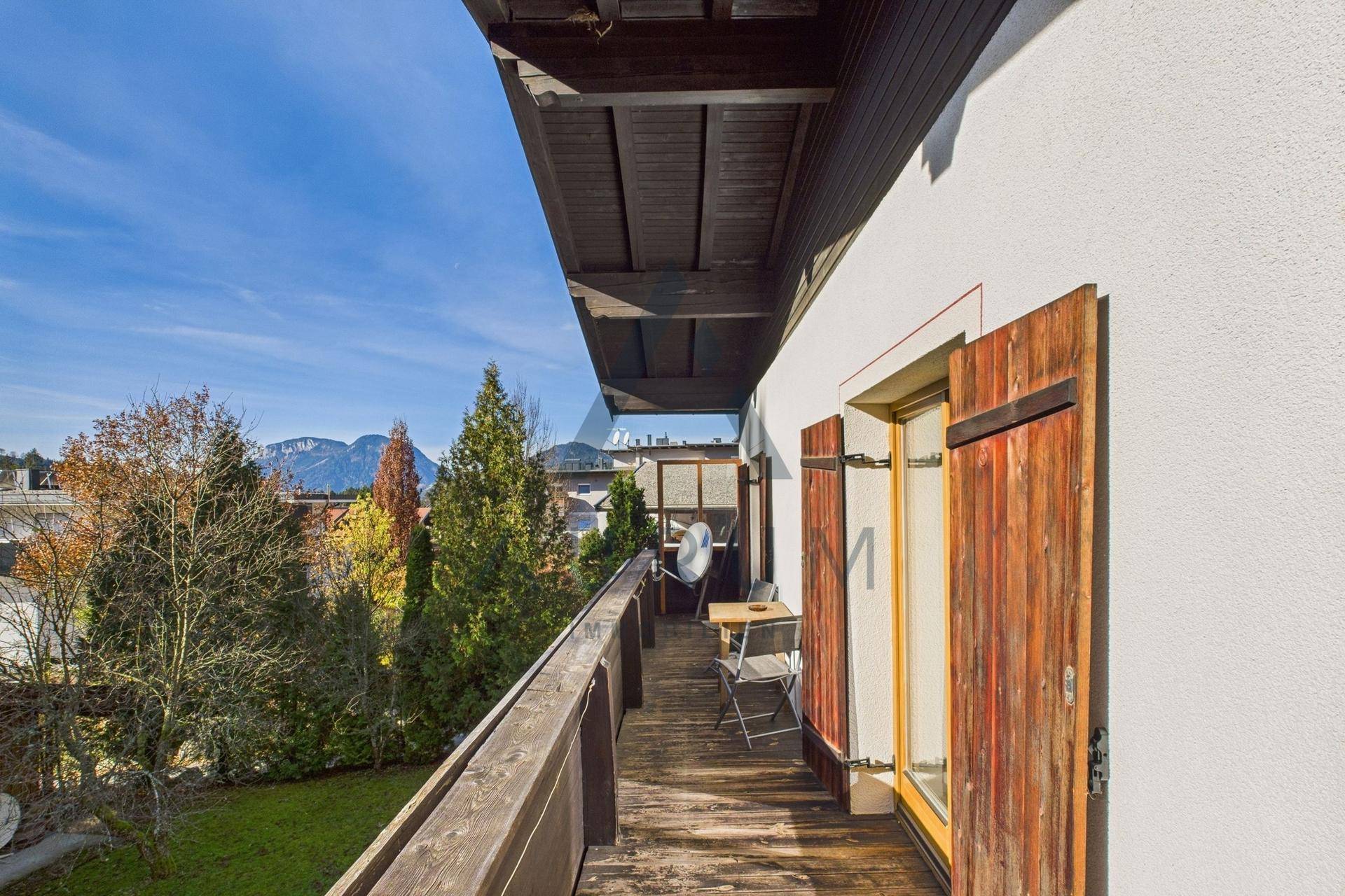 Langer Holzbalkon mit Sitzgelegenheiten und Bergblick in sonniger Umgebung.