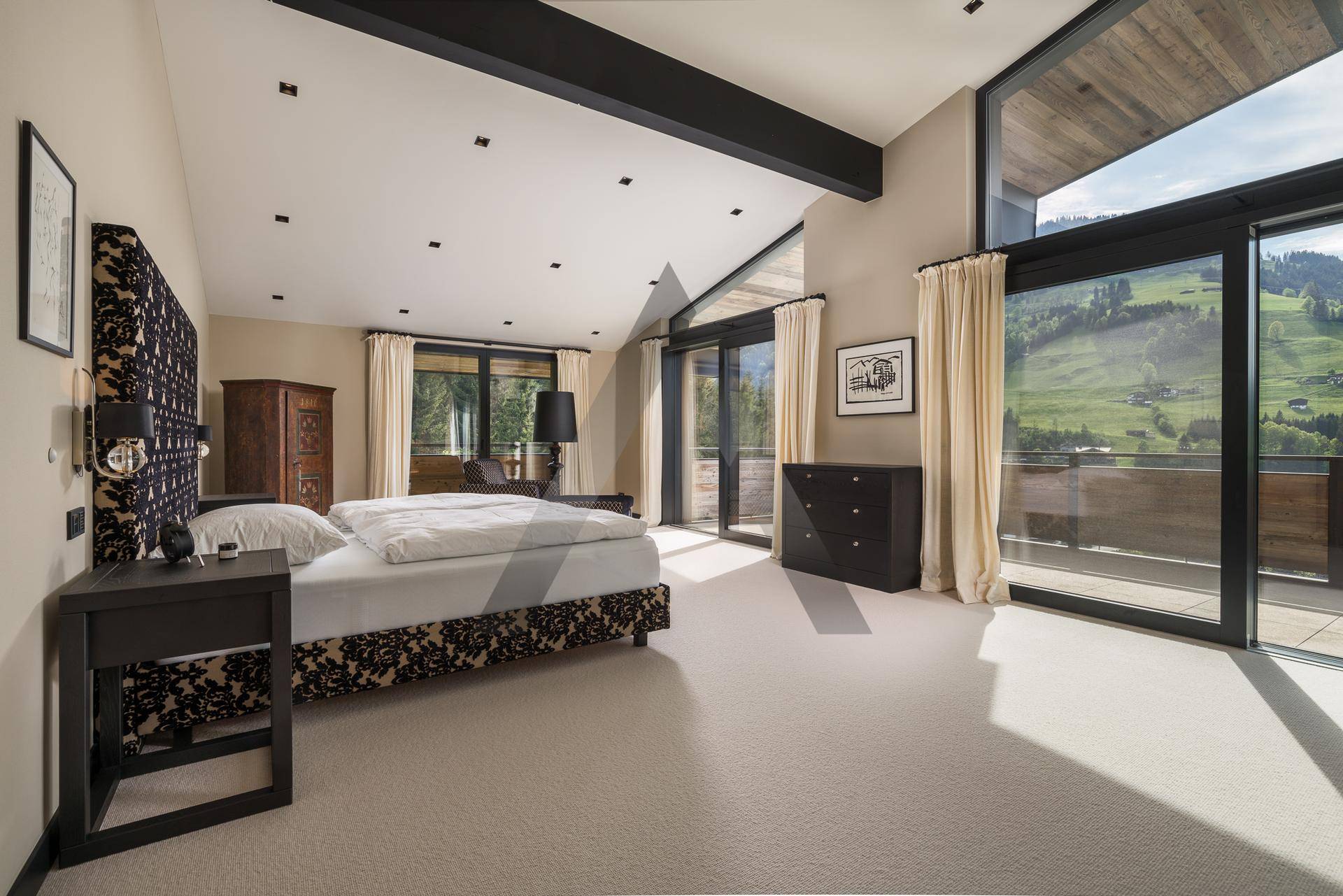 Helles Schlafzimmer mit Teppichboden, hohen Decken und Zugang zum Balkon mit Bergblick.