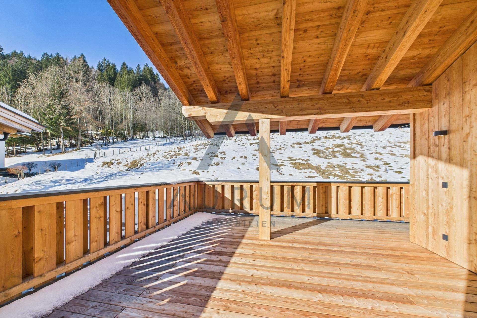 Große Holzterrasse mit Geländer und weitem Blick auf die verschneite Landschaft und den Wald.