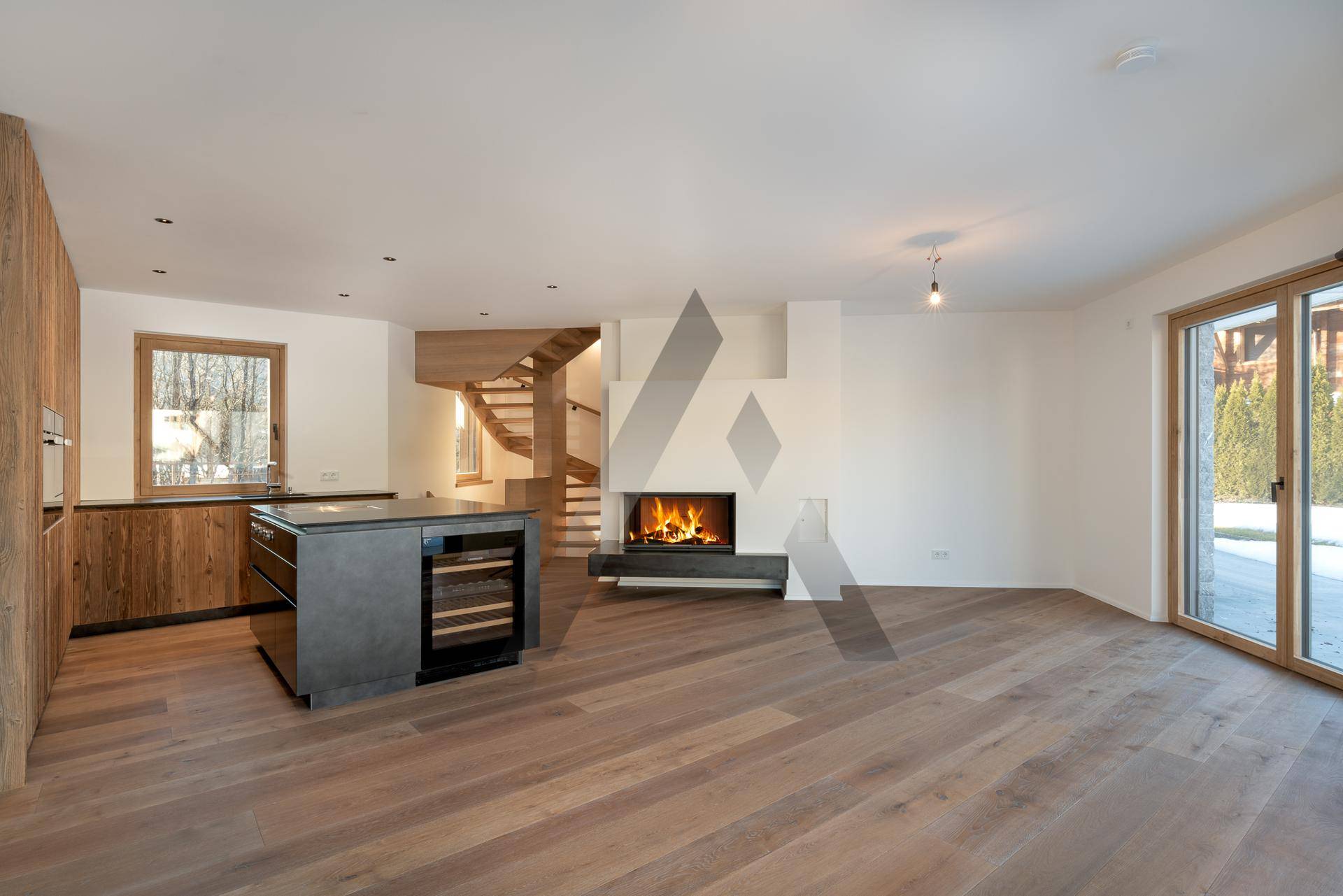 Offener Wohnbereich mit integrierter Küche, Kamin und Holzboden, ideal für geselliges Beisammensein.