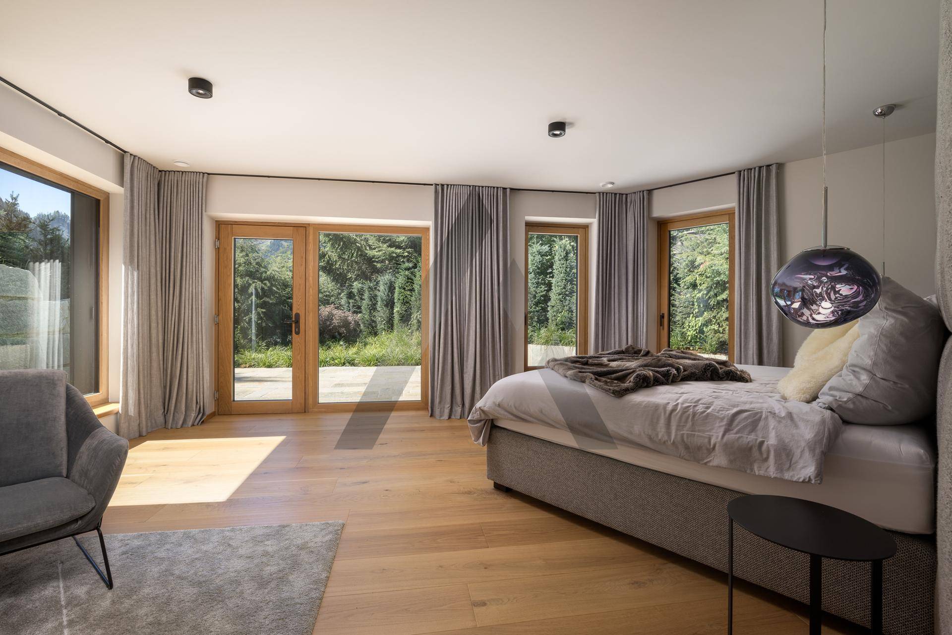 Helles Schlafzimmer mit Holzboden und großen Fenstern, die einen schönen Blick ins Grüne bieten.
