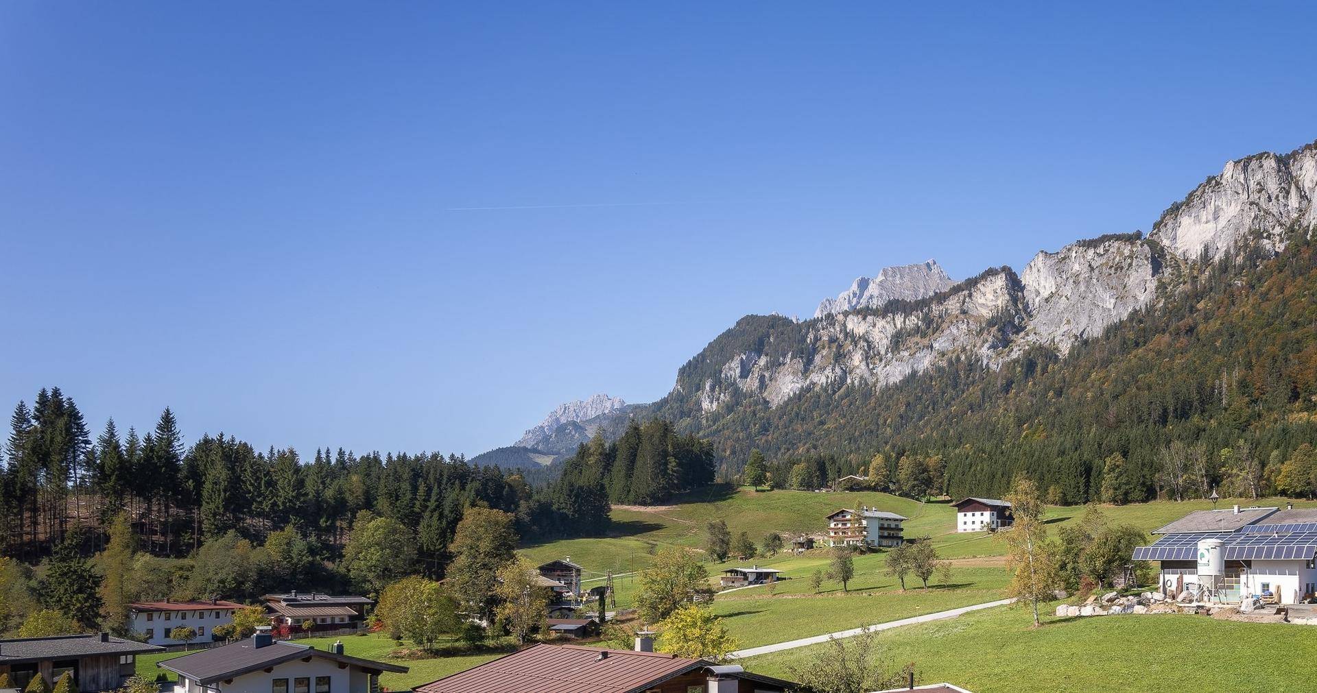 Panoramablick auf eine weite Berglandschaft mit Wäldern und vereinzelten Häusern unter klarem Himmel.