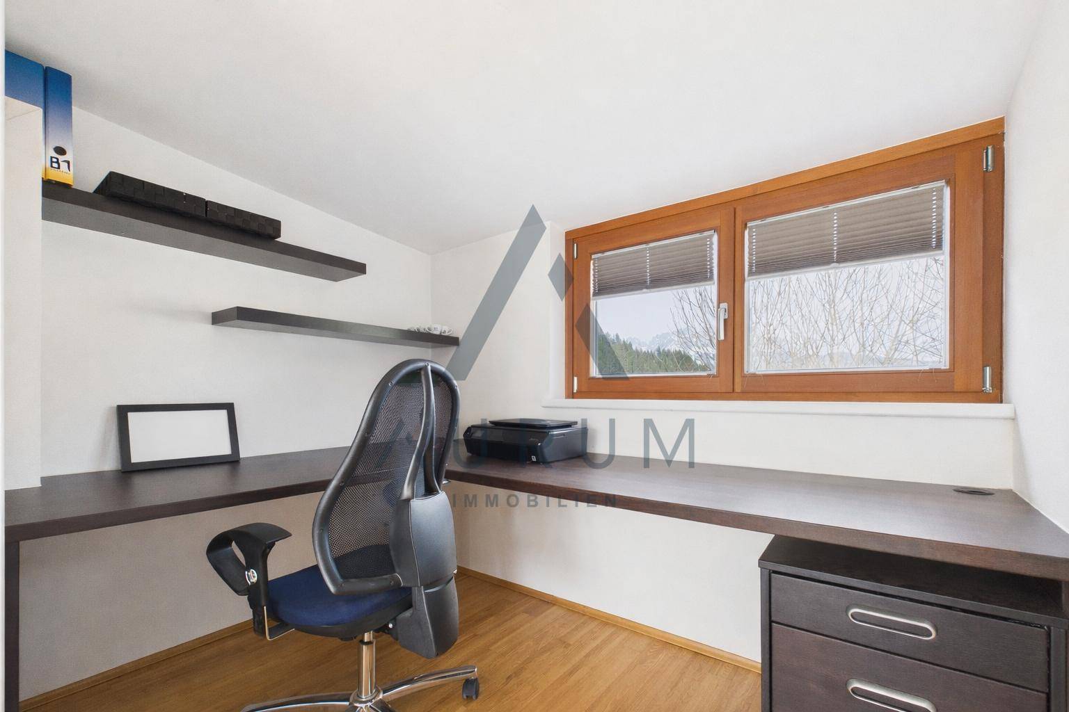 Funktionales Heimbüro mit großem Schreibtisch, Regalen und Fenster mit Ausblick.