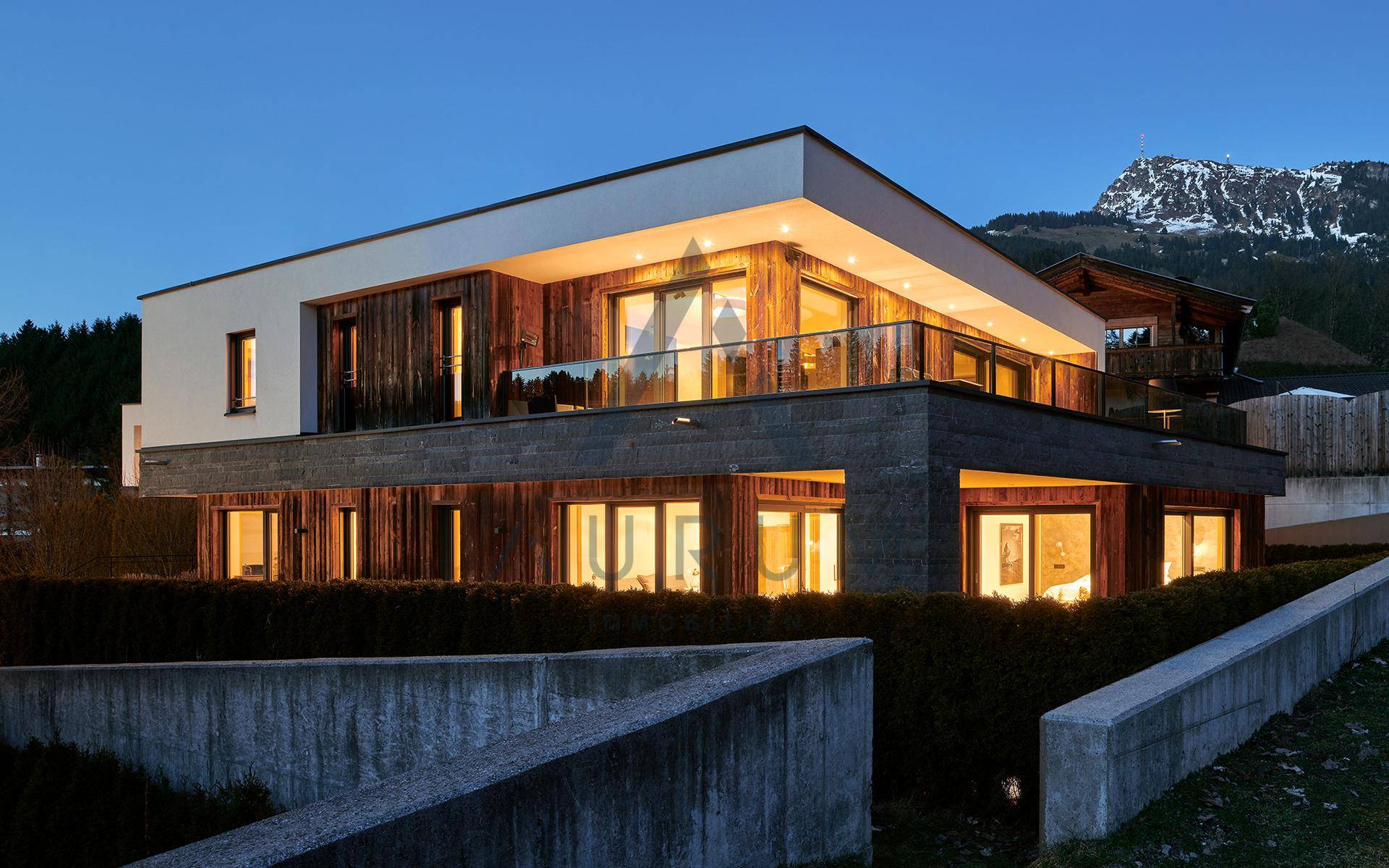 Modernes Gebäude mit Holzfassade und großen Fenstern, umgeben von Natur.