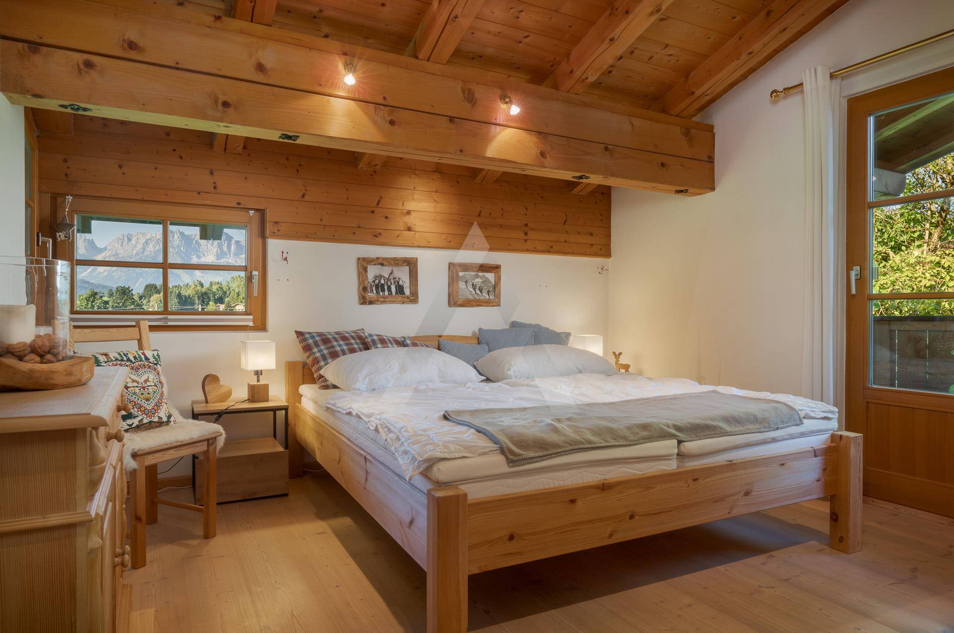 Schlafzimmer im Landhausstil mit Holzbett, Holzbalkendecke und Bergblick.
