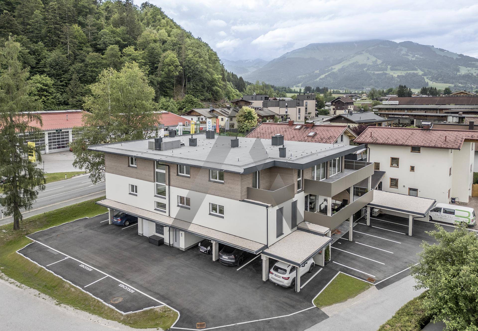 Luftaufnahme eines modernen Mehrfamilienhauses mit Parkplätzen und Carports in einer grünen Umgebung.