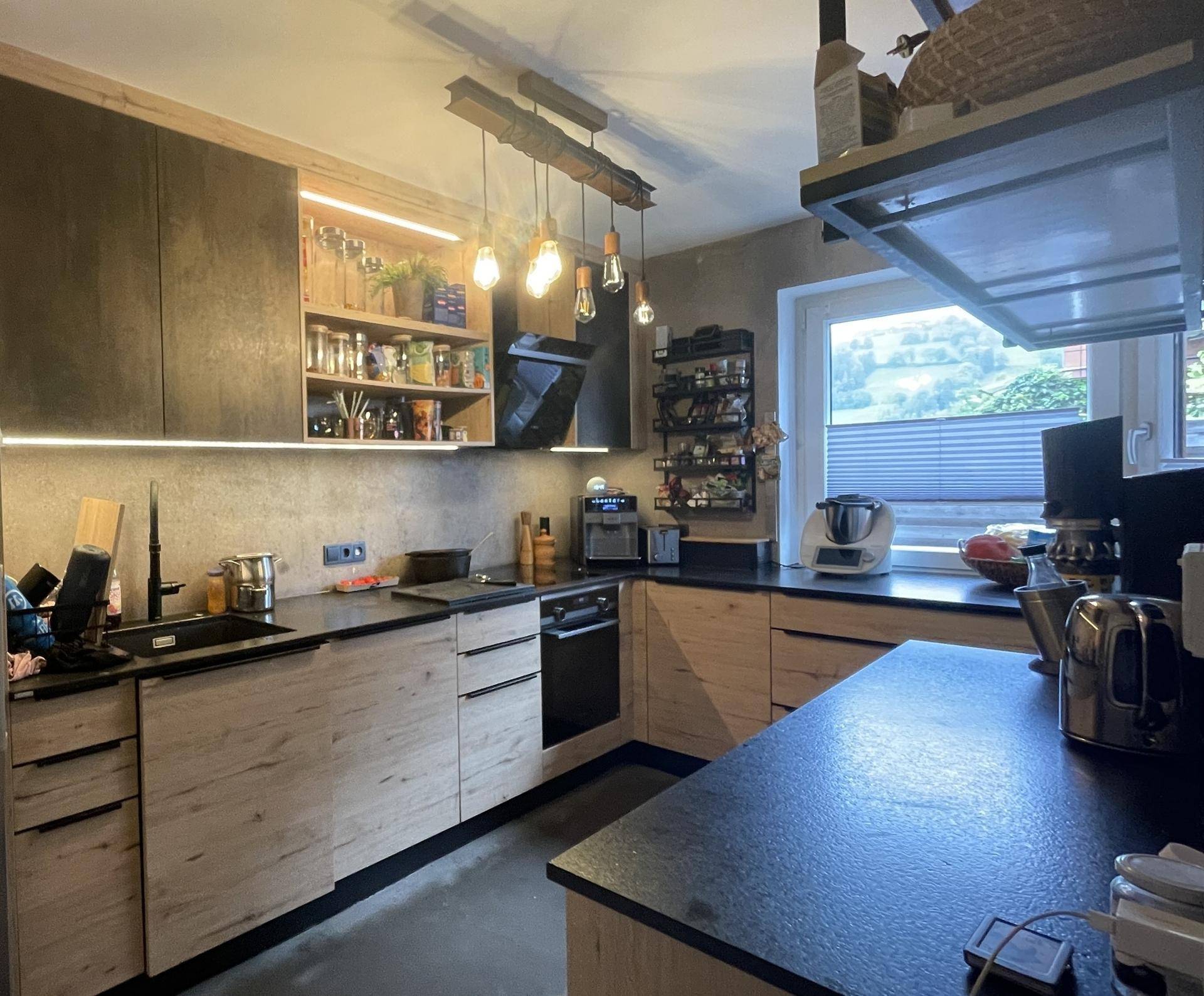 Moderne Küche mit Holzfronten, dunklen Arbeitsplatten und integrierten Geräten.