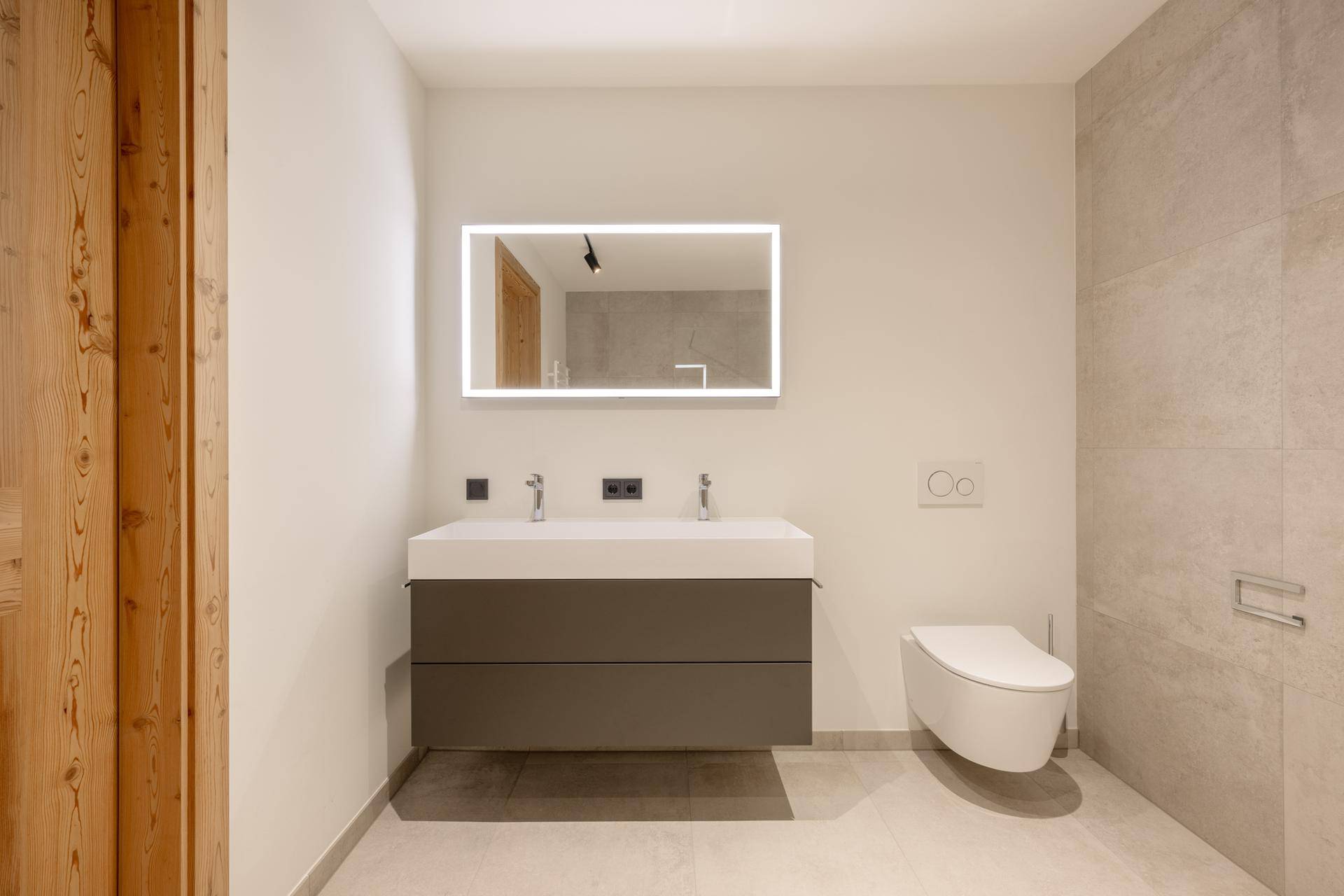 Modernes Badezimmer mit Doppelwaschbecken, wandhängendem WC und beleuchtetem Spiegel.