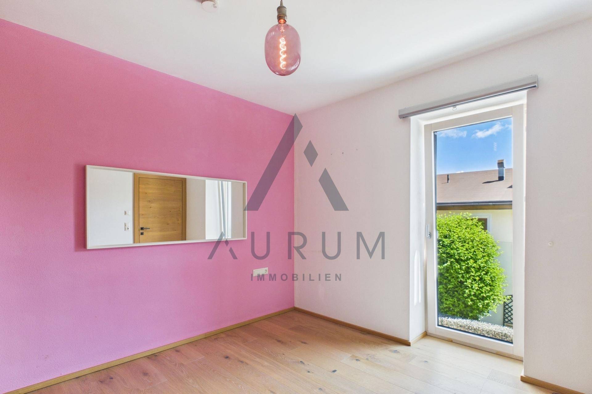 Helles Schlafzimmer mit rosa Akzentwand, Holzboden und Zugang zu einem kleinen Balkon.