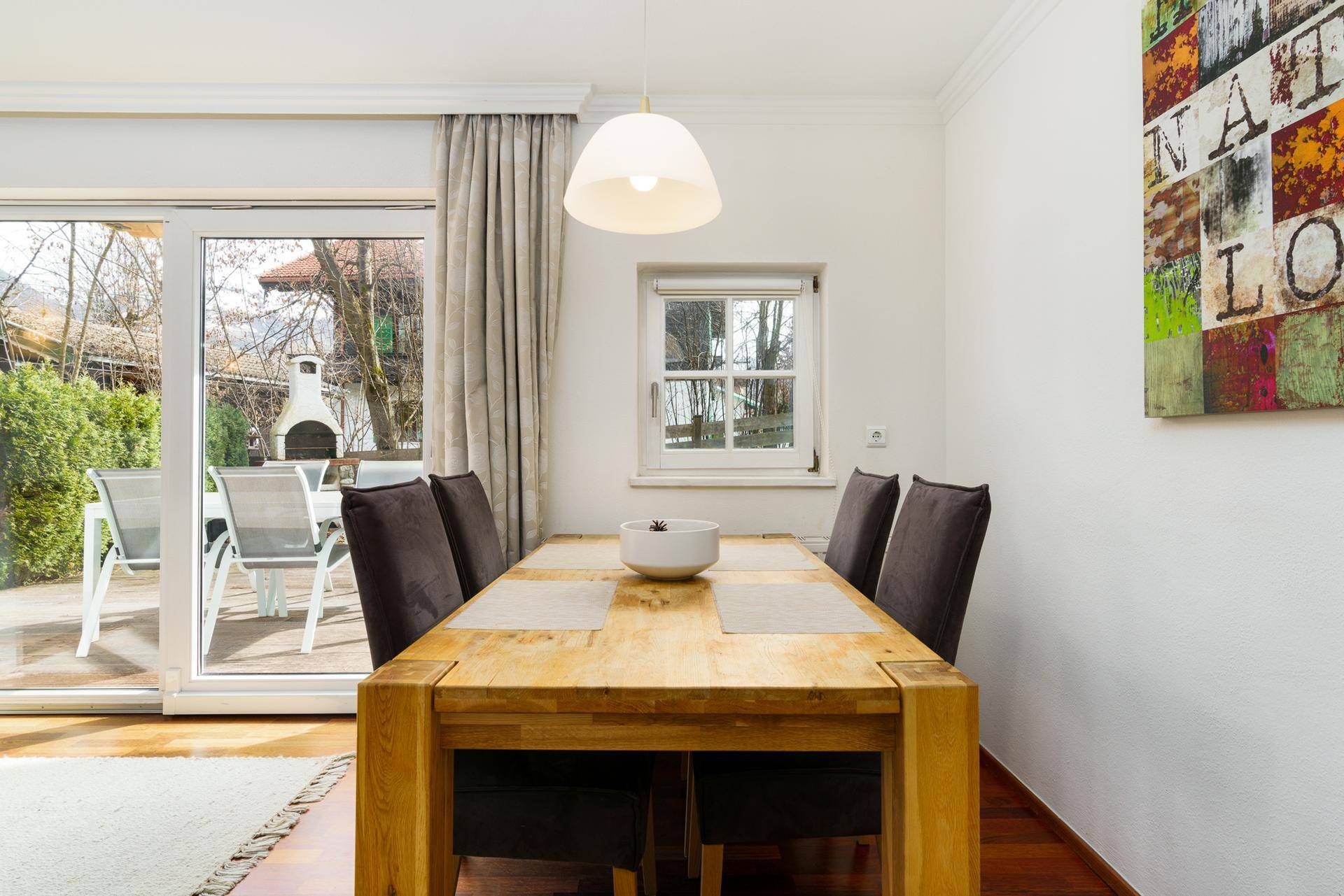 Nahaufnahme des Essbereichs mit Holztisch und Stühlen, Fenster und Schiebetür zur Außenterrasse.