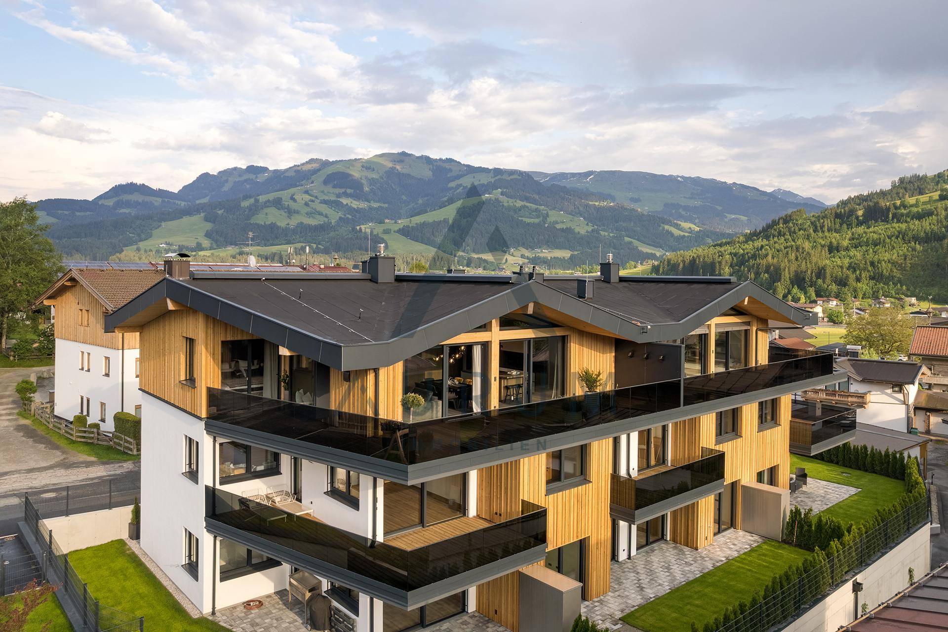 Modernes Mehrfamilienhaus mit Holzfassade, Balkonen und Bergblick in alpiner Umgebung.