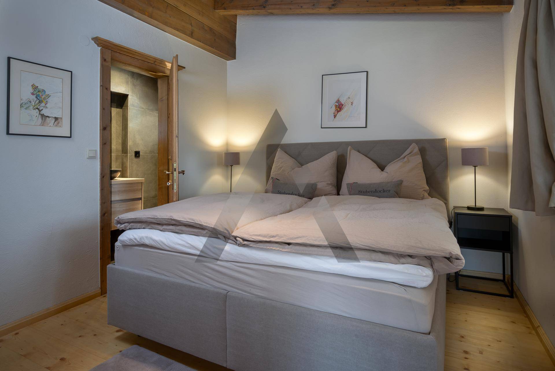 Komfortables Schlafzimmer mit Holzboden, sichtbaren Balken und direktem Zugang zum Badezimmer.