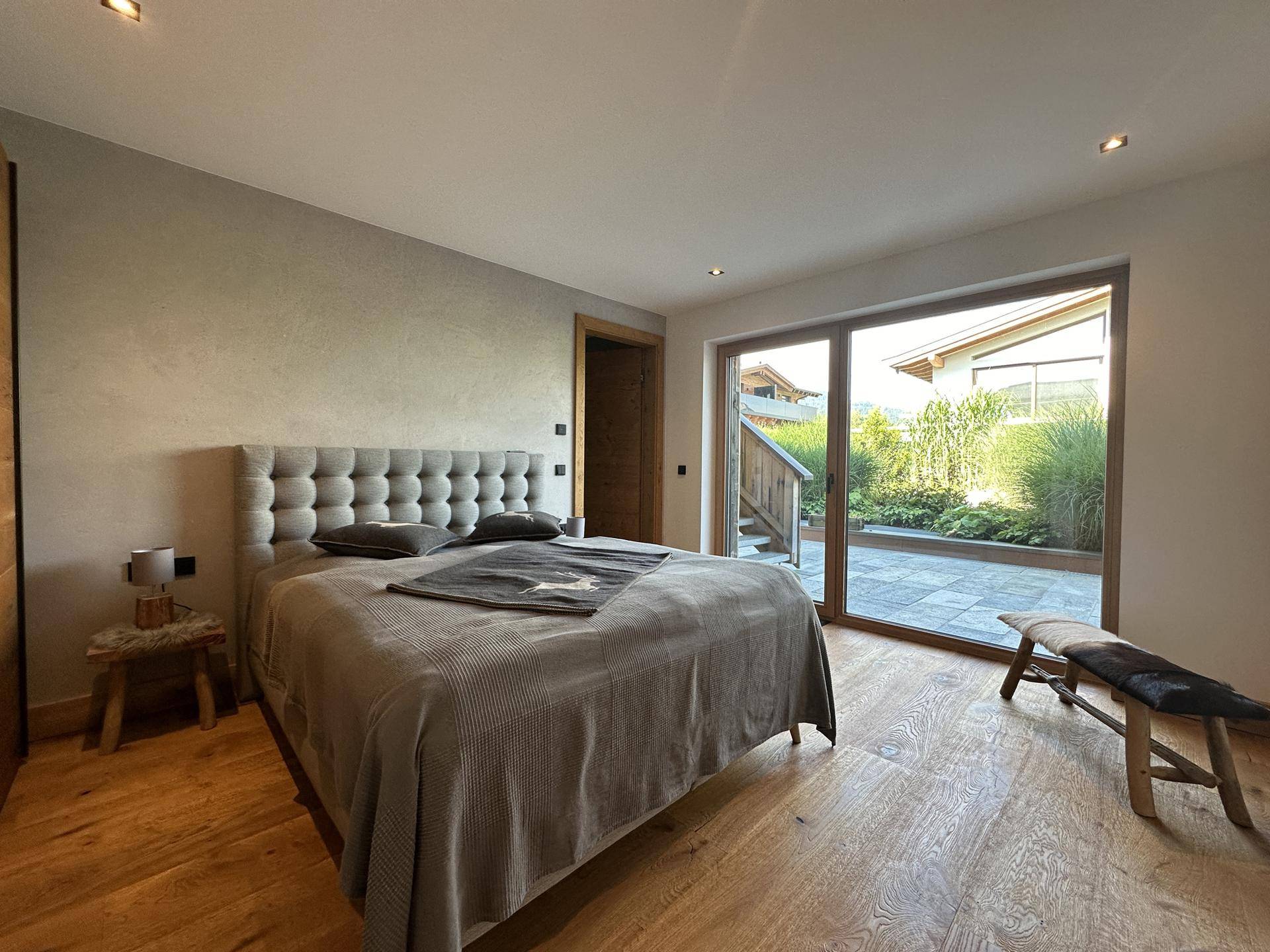 Schlafzimmer mit Holzboden, gepolstertem Bett und Zugang zu einer Terrasse.