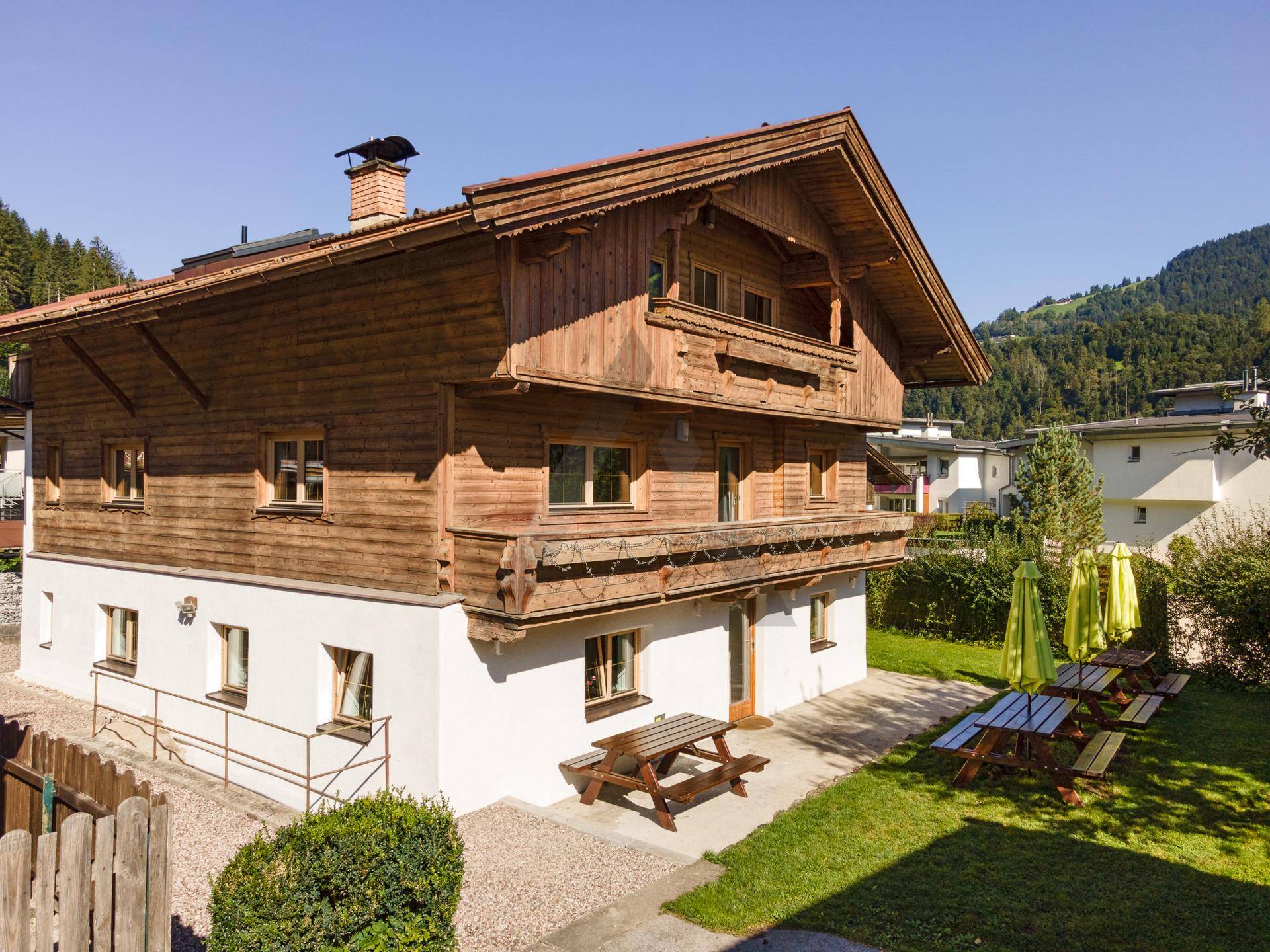 Traditionelles Holzhaus mit weißem Sockel und großem Gartenbereich mit Picknicktischen.