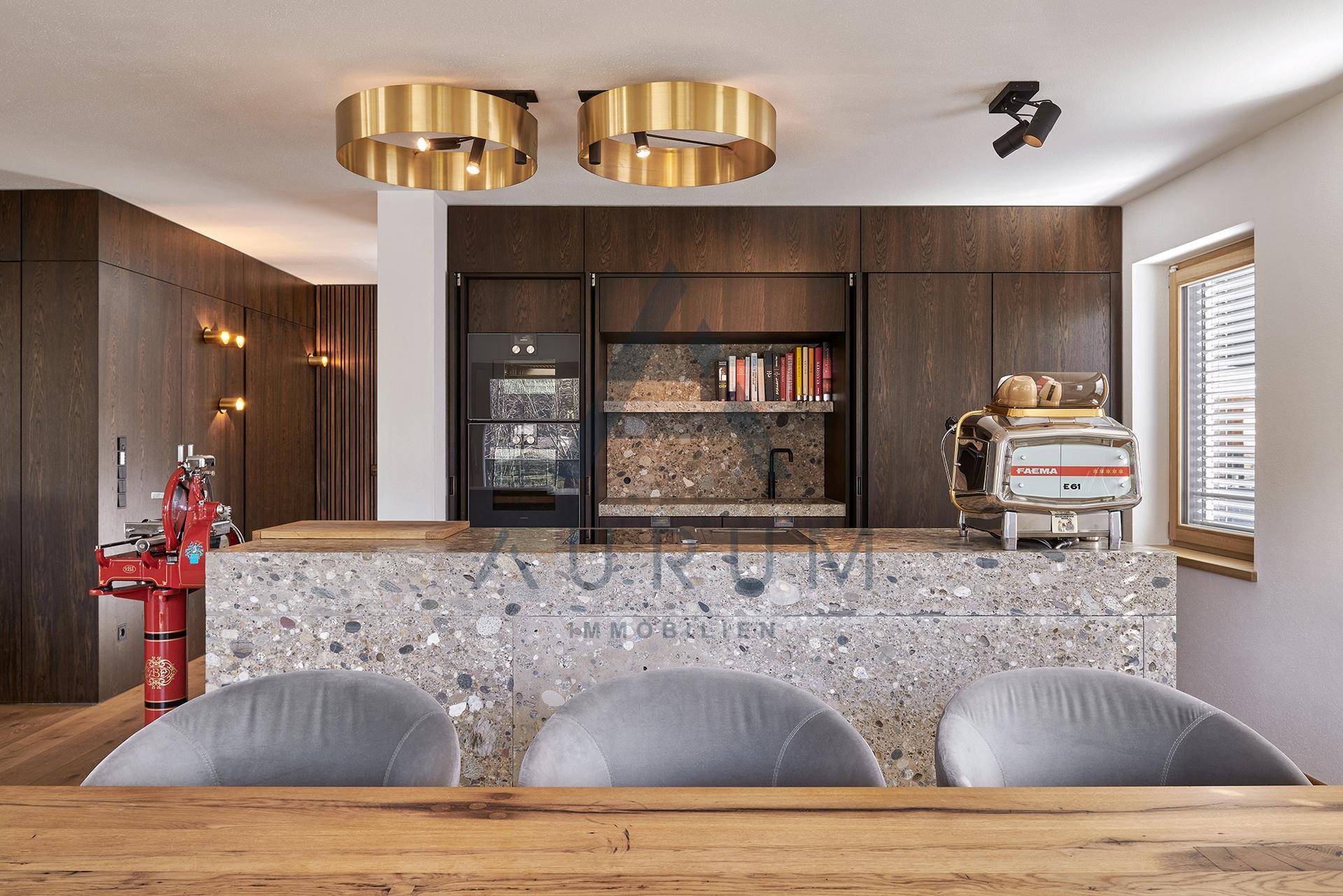 Moderne Küche mit Stein-Arbeitsplatte, integrierten Geräten und goldenen Leuchten.