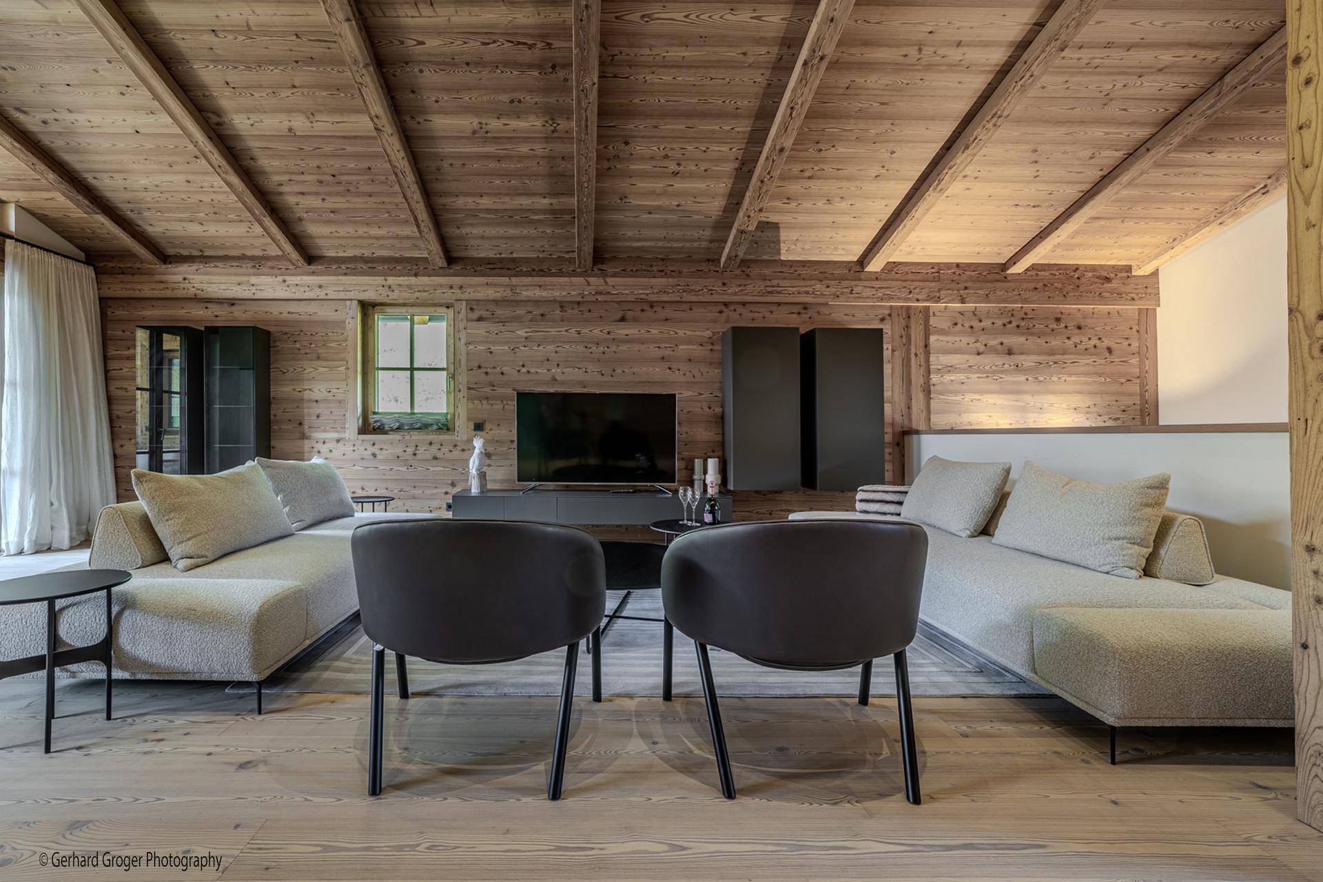 Gemütliches Wohnzimmer mit Holzvertäfelung, bequemen Sofas und Holzbalkendecke.