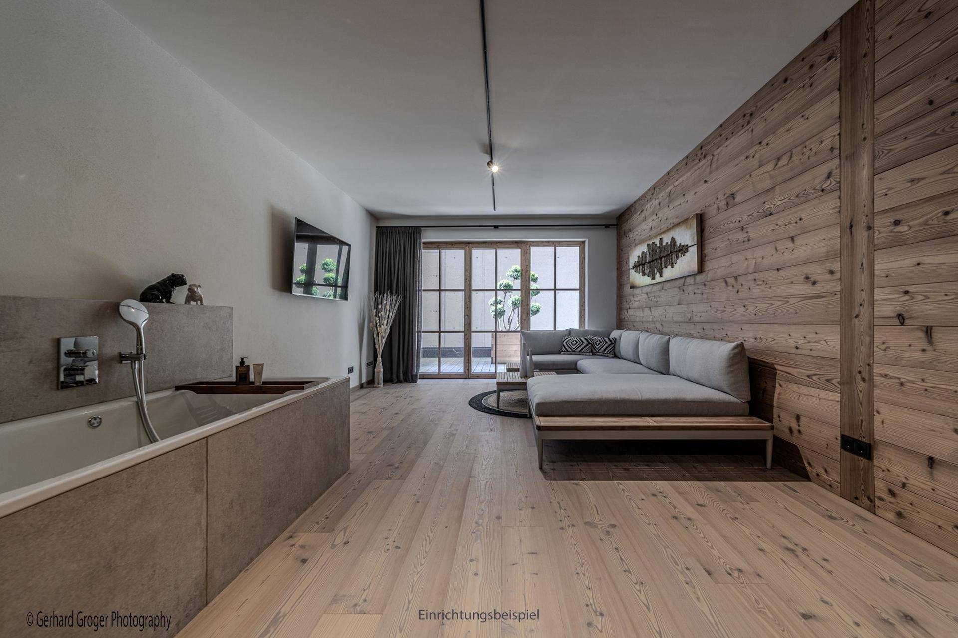 Offener Wohnbereich mit Holzwand, Sofa und einer integrierten Badewanne.