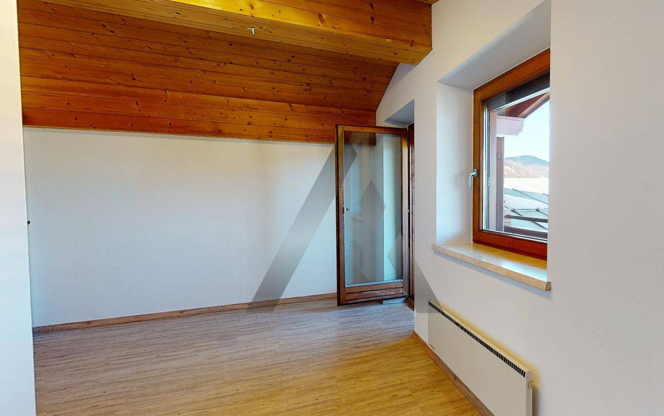 Dachzimmer mit sichtbaren Holzbalken, schrägen Decken und einem Fenster mit Bergblick.