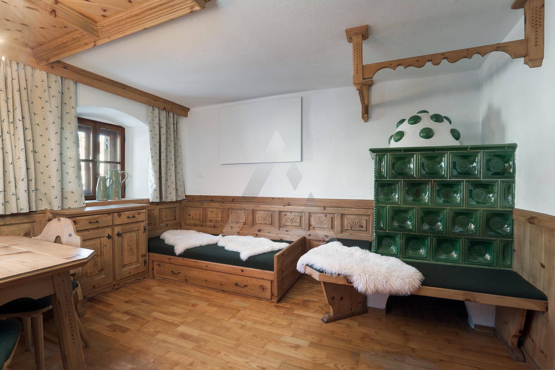 Rustikaler Wohnbereich mit traditionellem Kachelofen, Holzbänken und Holzboden.