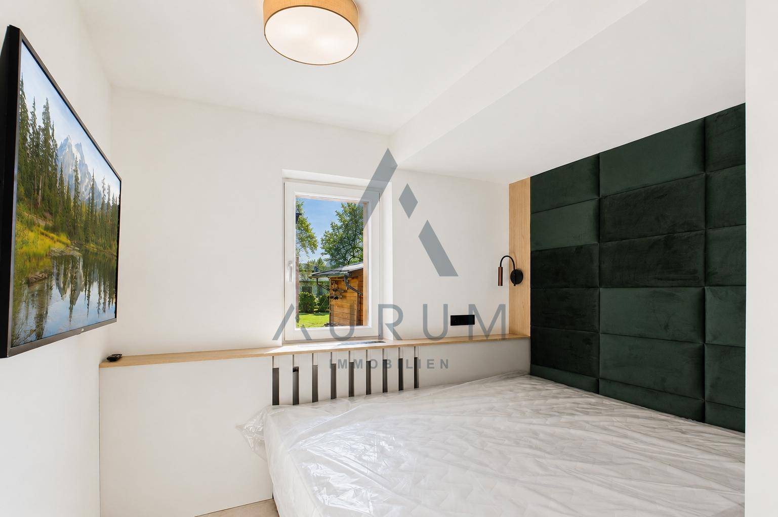 Gemütliches Schlafzimmer mit modernem Kopfteil, Fernseher und Blick ins Grüne.