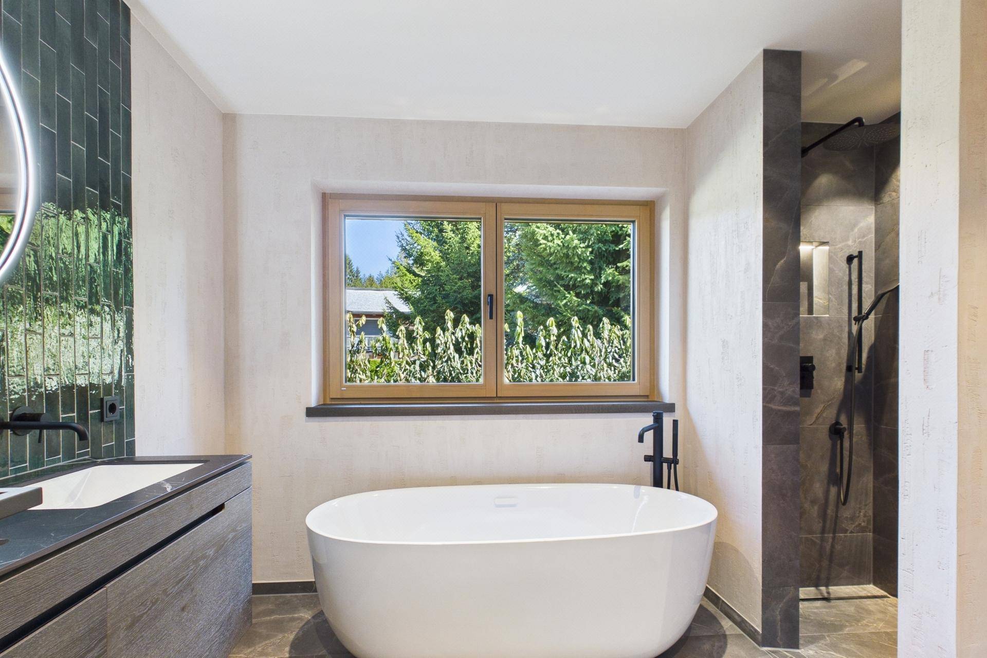Modernes Badezimmer mit freistehender Badewanne, Dusche und Fenster mit Grünblick.