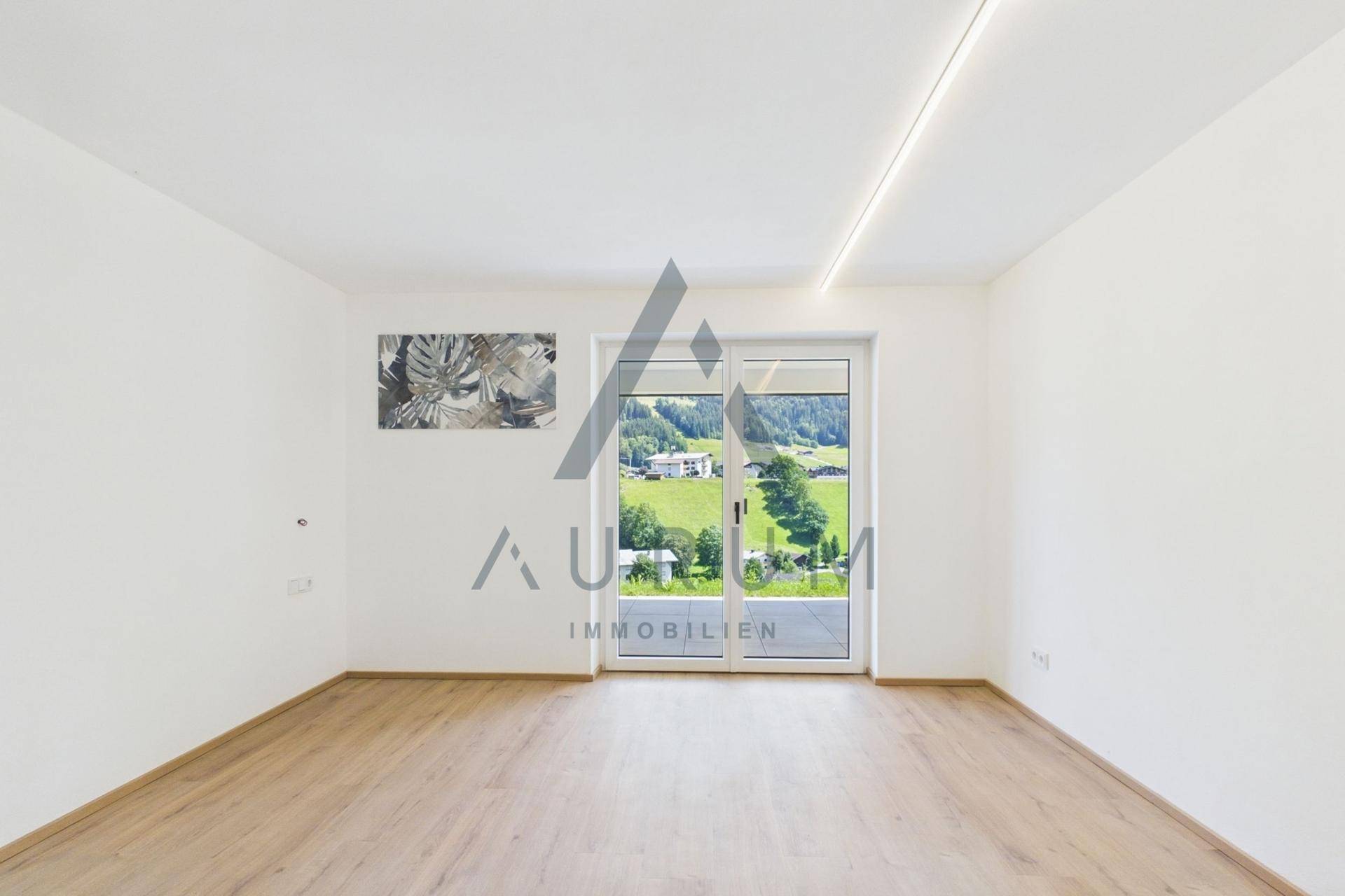 Lichtdurchflutetes Zimmer mit Holzboden und großem Fenster mit Bergblick.