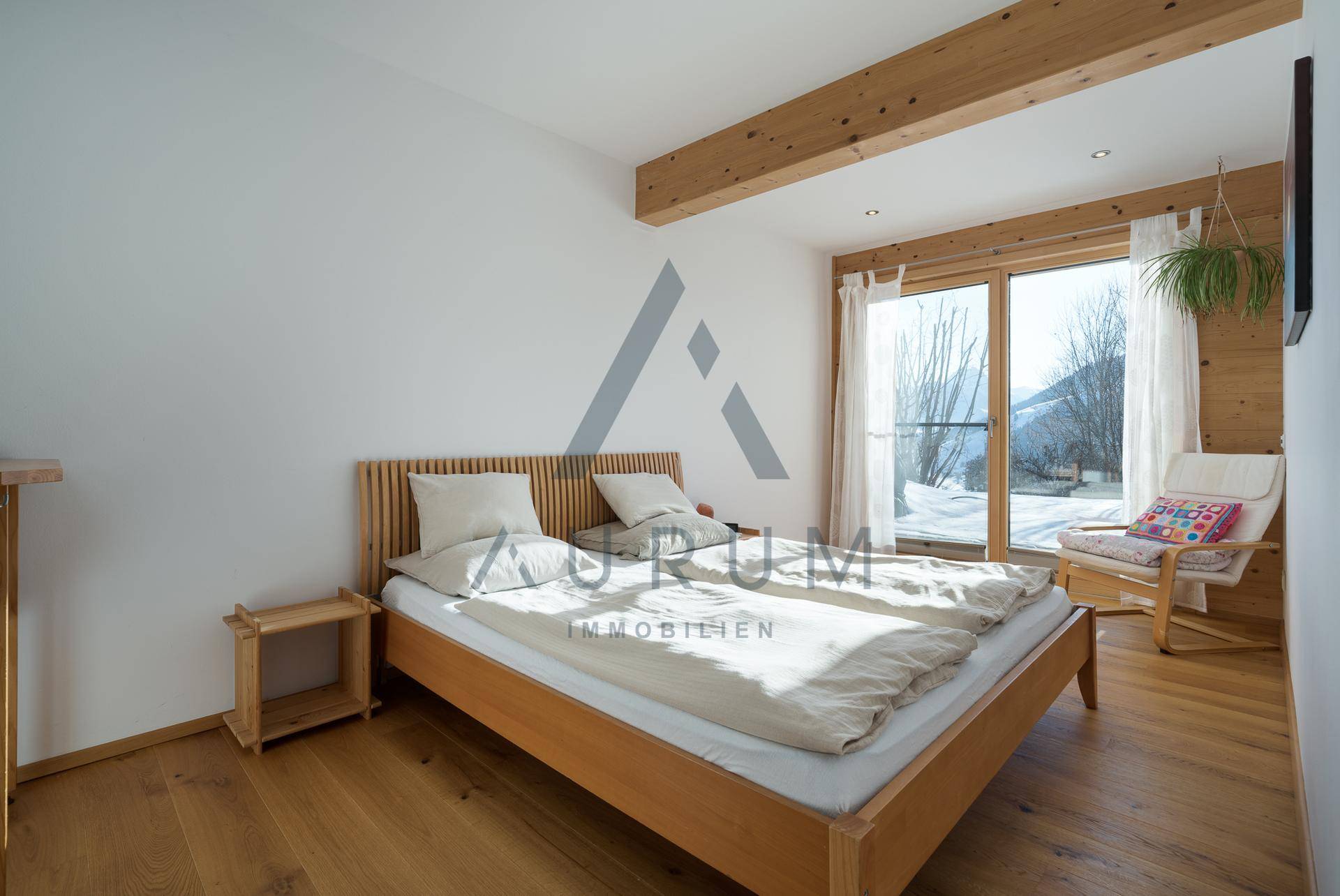 Helles Schlafzimmer mit Holzbalken, Holzboden und Zugang zu einem Balkon mit Bergblick.