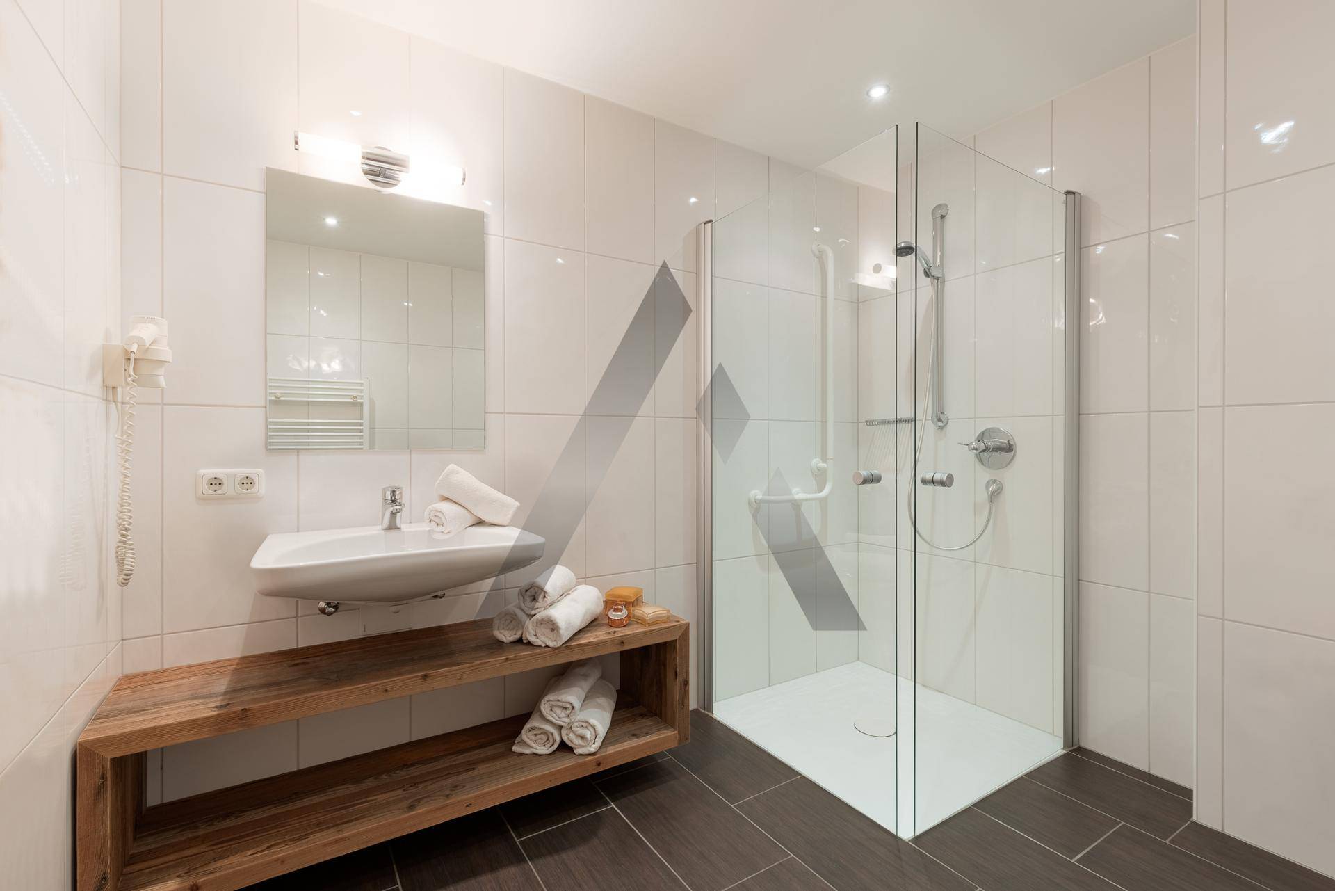 Modernes Badezimmer mit begehbarer Dusche, weißen Fliesen und Holzwaschtisch.
