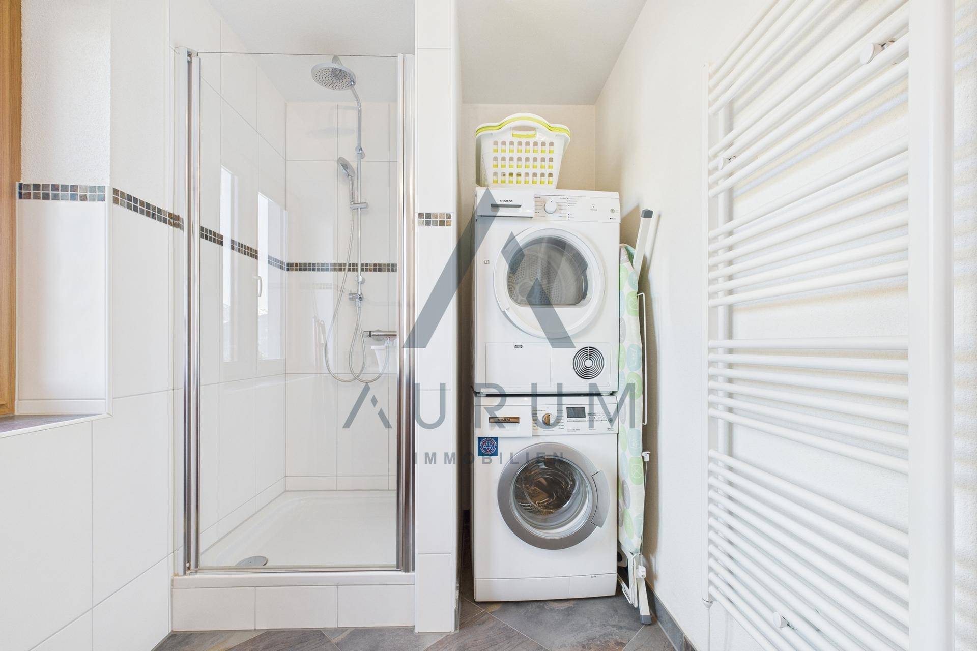 Modernes Badezimmer mit Duschkabine, Waschmaschine und Trockner, praktisch und funktional eingerichtet.