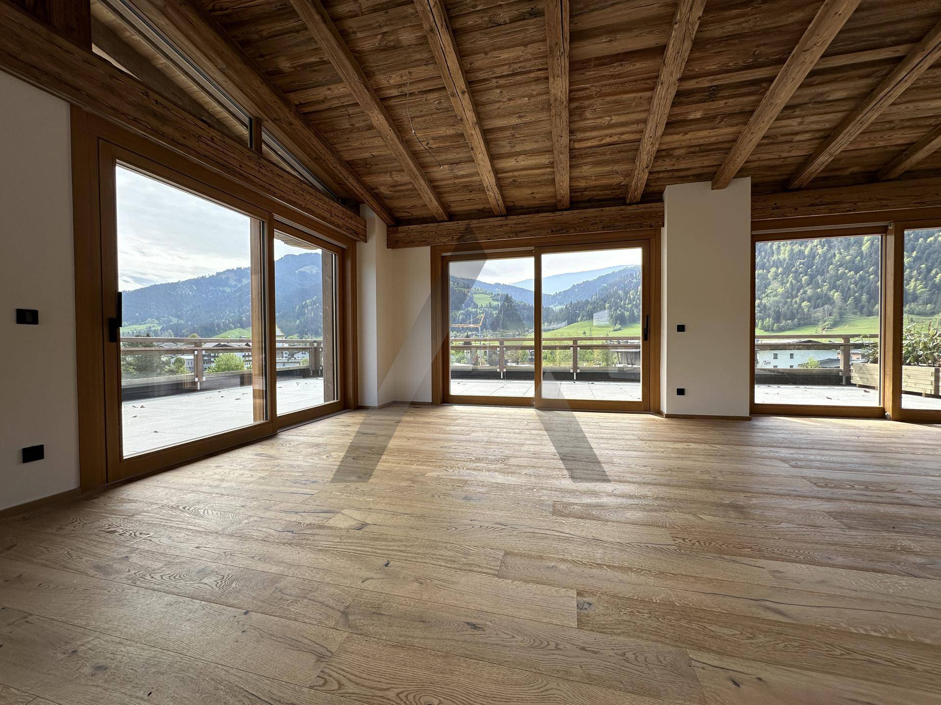 Großzügiger Wohnraum mit Holzboden, Holzbalkendecke und Panoramafenstern mit Bergblick.