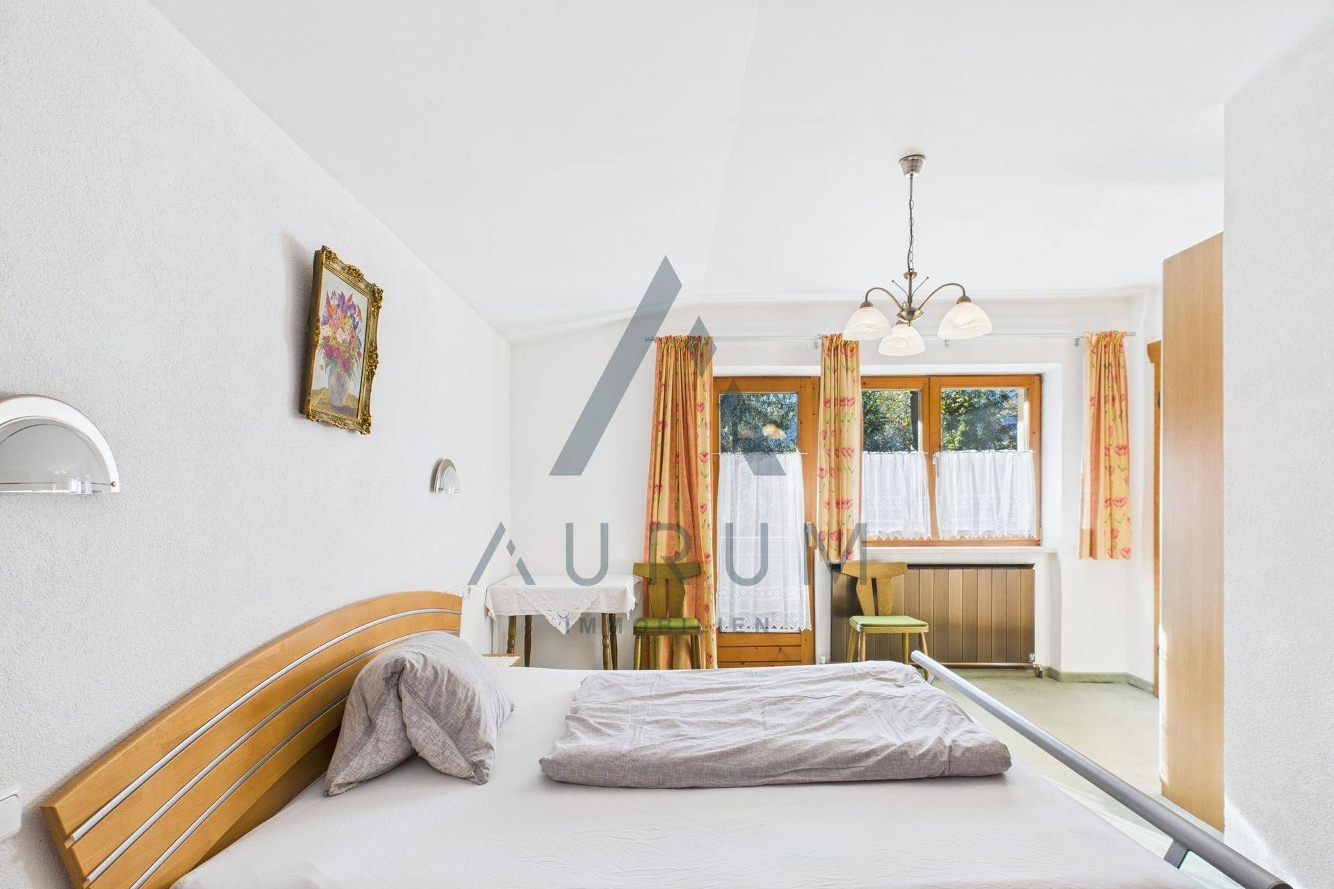 Schlafzimmer mit Einzelbett, Holzboden und Fenstern, die viel Tageslicht hereinlassen.