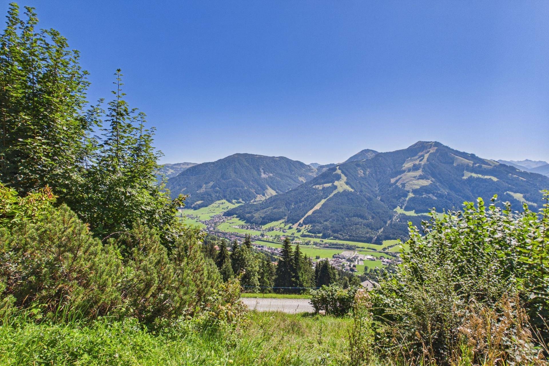 Panoramablick auf die alpine Landschaft mit einem Dorf im Tal und bewaldeten Hängen.