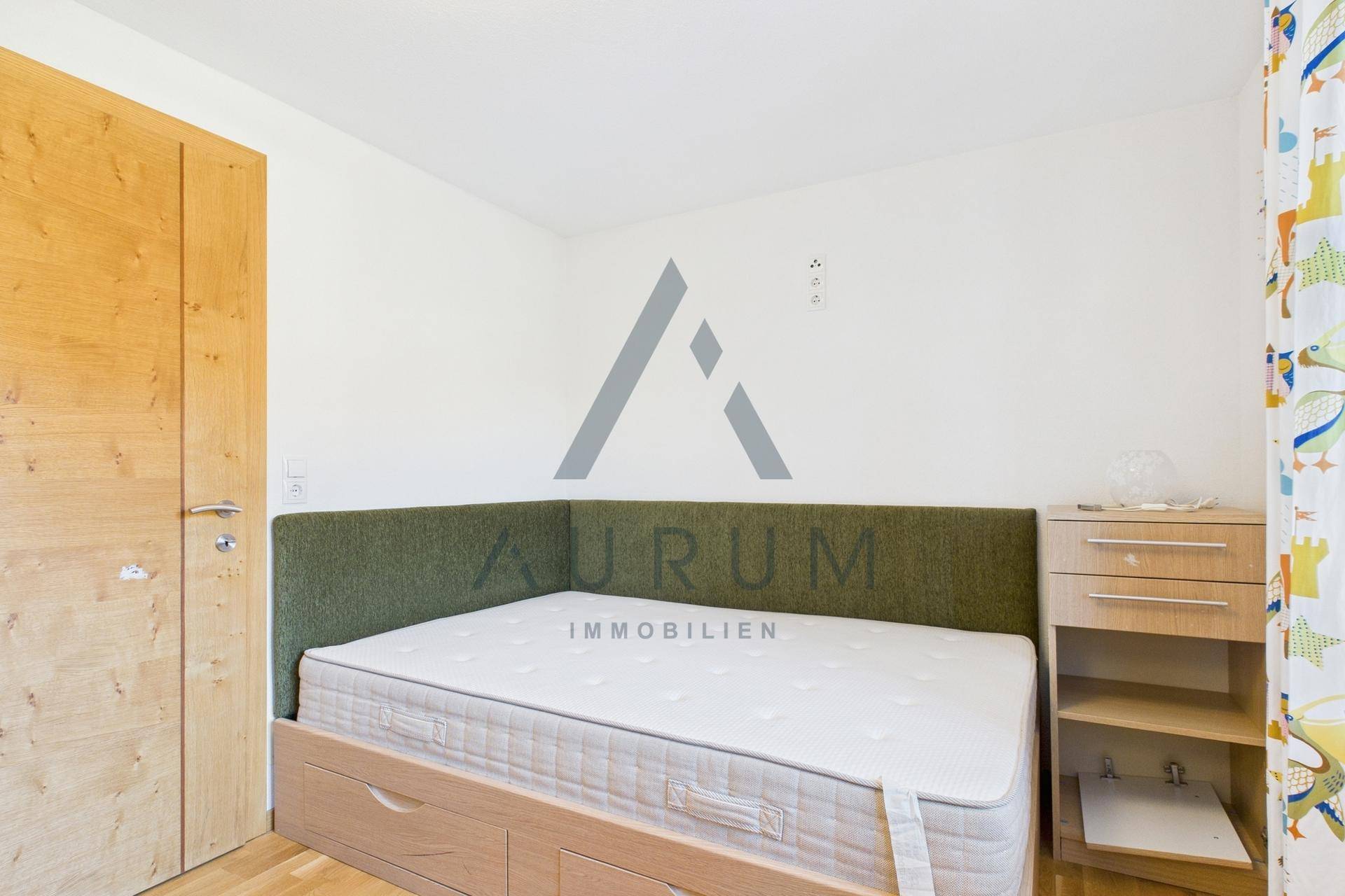 Helles Schlafzimmer mit Einzelbett, Holzboden und einem Fenster mit bunten Vorhängen.