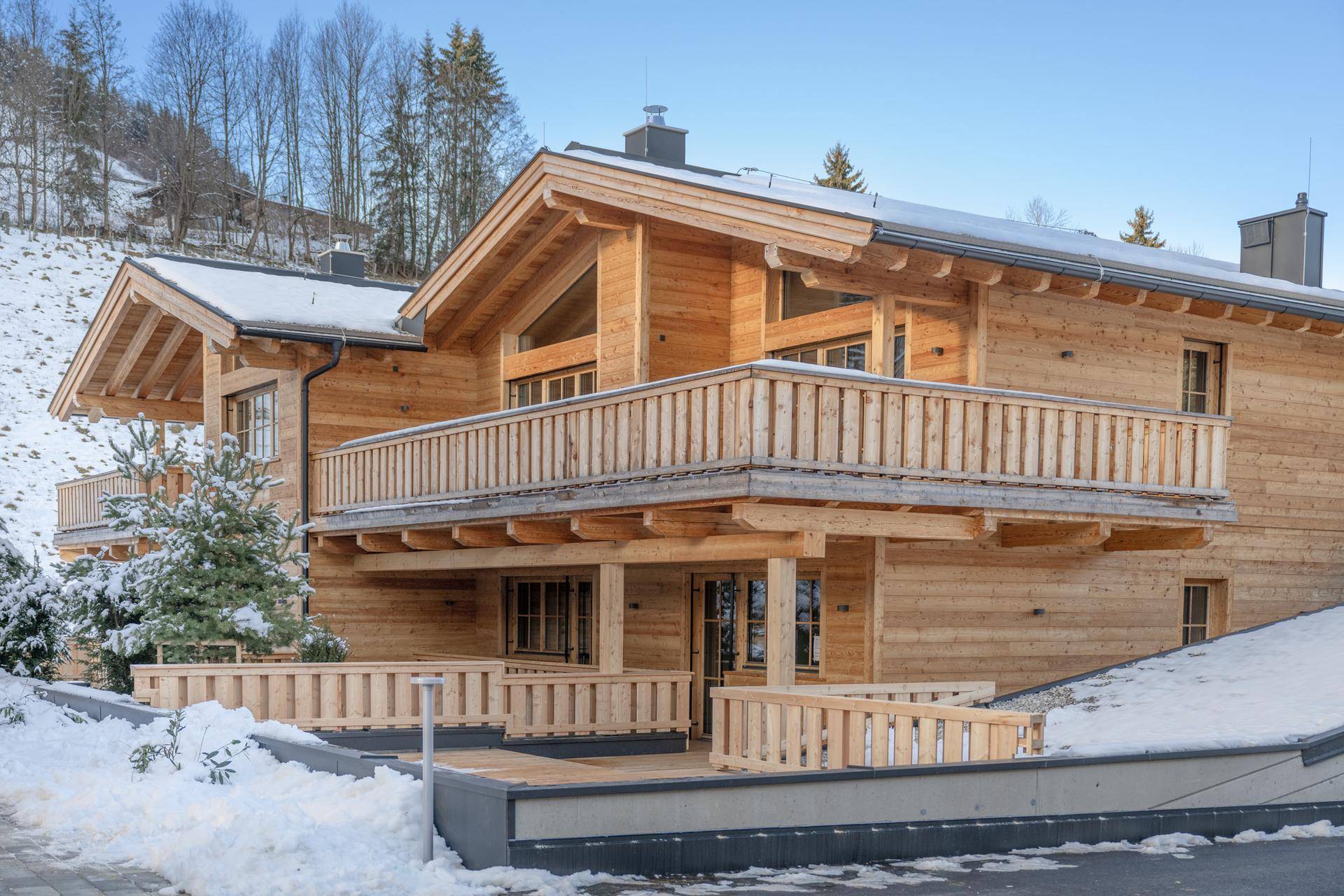 Attraktives Holzhaus im Chalet-Stil mit Balkonen und Terrassen in verschneiter Berglandschaft.