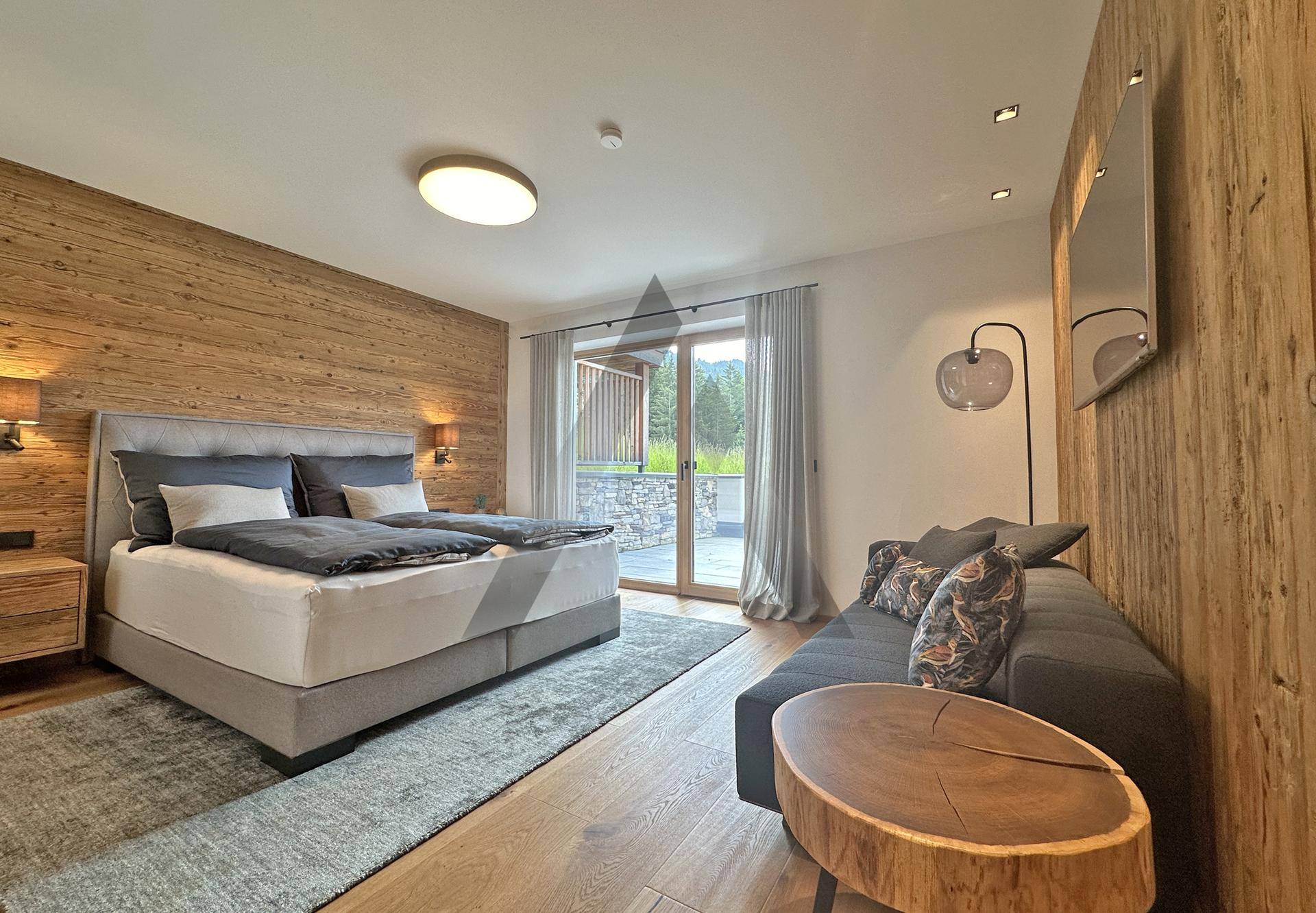 Gemütliches Schlafzimmer mit Holzwänden, Doppelbett und Zugang zu einer Terrasse.