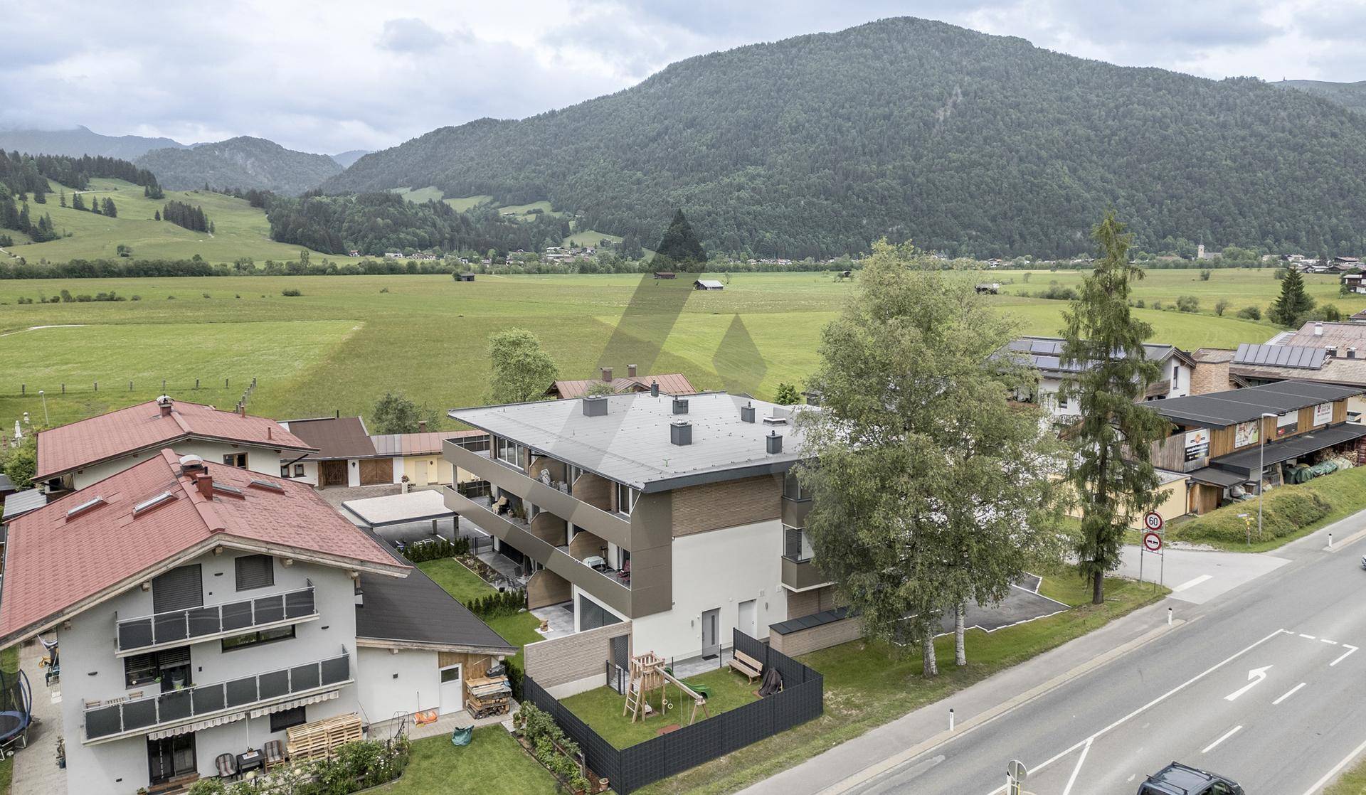 Luftaufnahme eines modernen Wohngebäudes in ländlicher Umgebung mit Spielplatz und viel Grün.