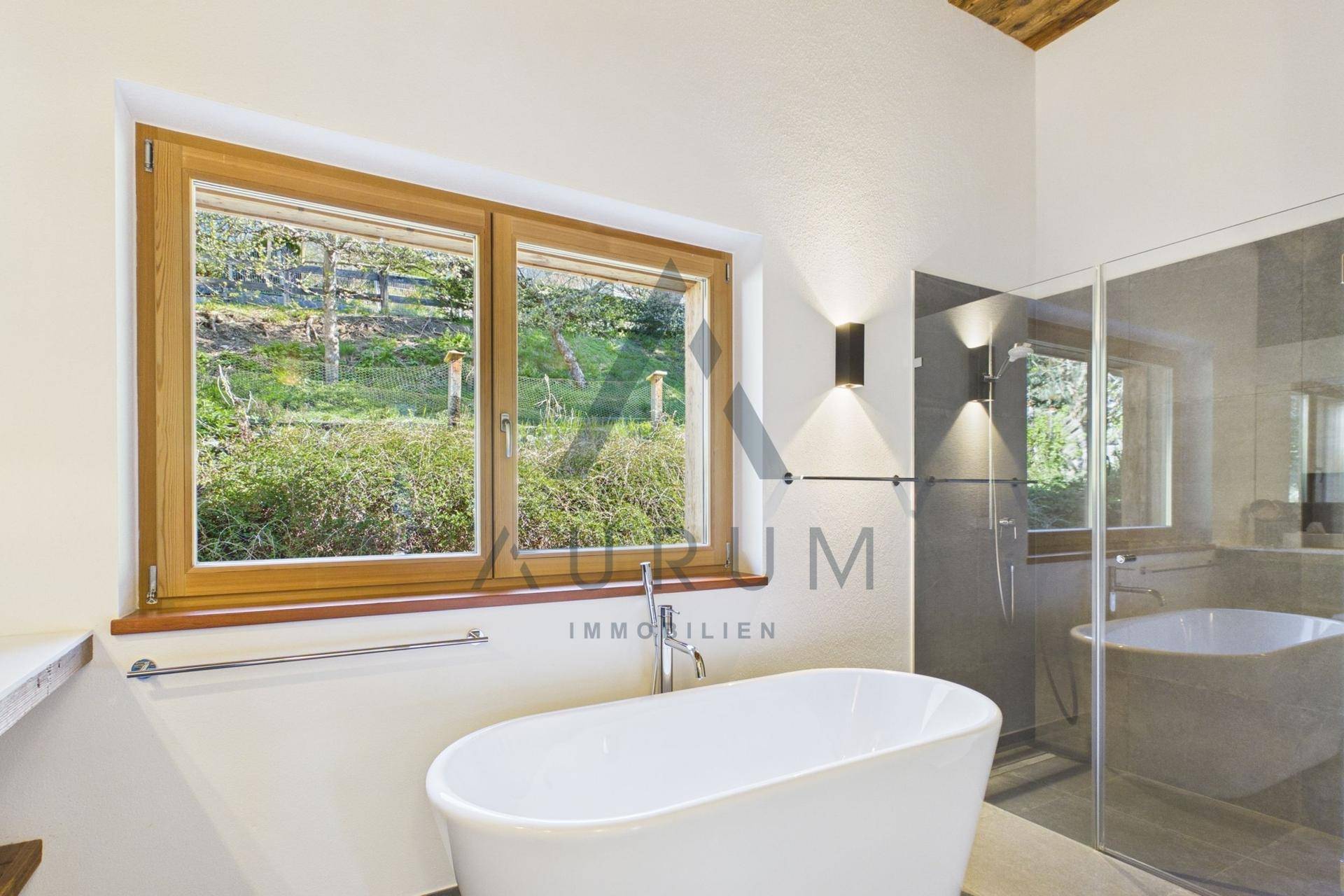 Helles Badezimmer mit freistehender Badewanne und großem Fenster mit Blick ins Grüne.