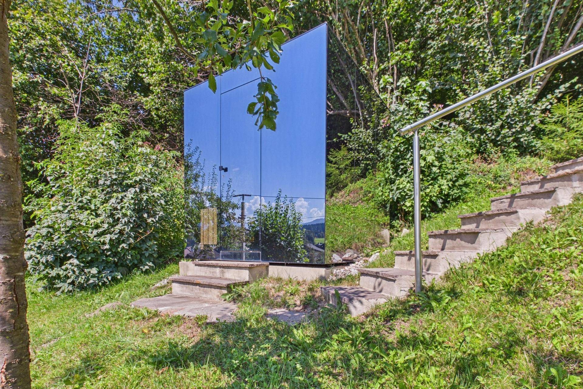 Modernes, verspiegeltes Gebäude im Grünen mit Treppe, das sich in die Landschaft einfügt.
