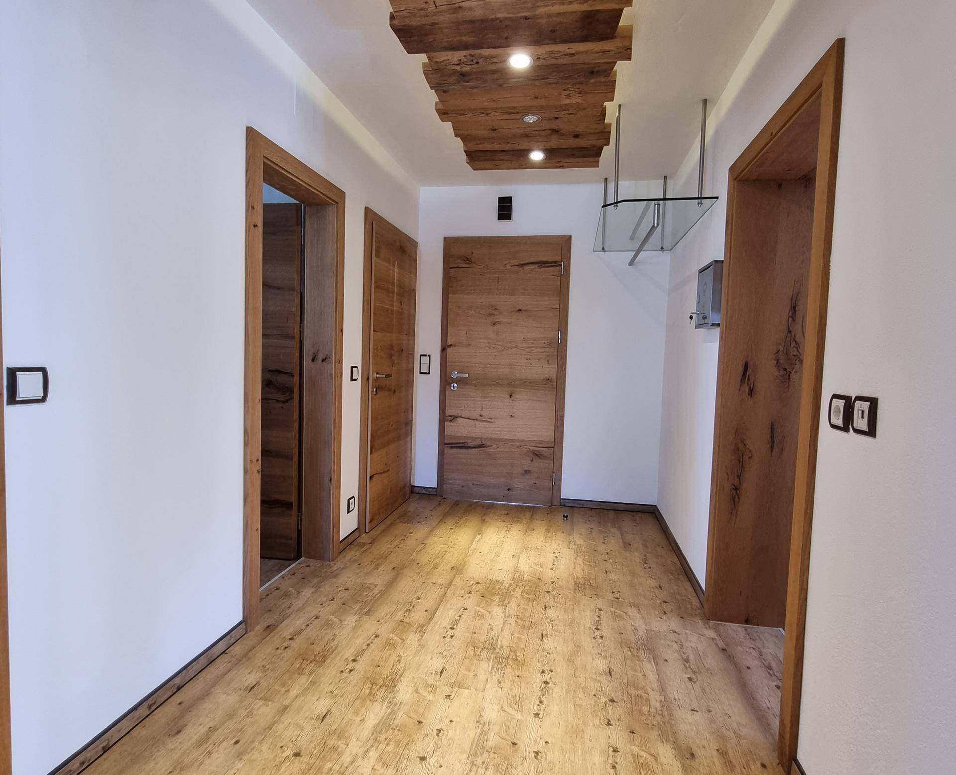 Heller Flur mit Holztüren, Holzakzenten an der Decke und modernem Bodenbelag.