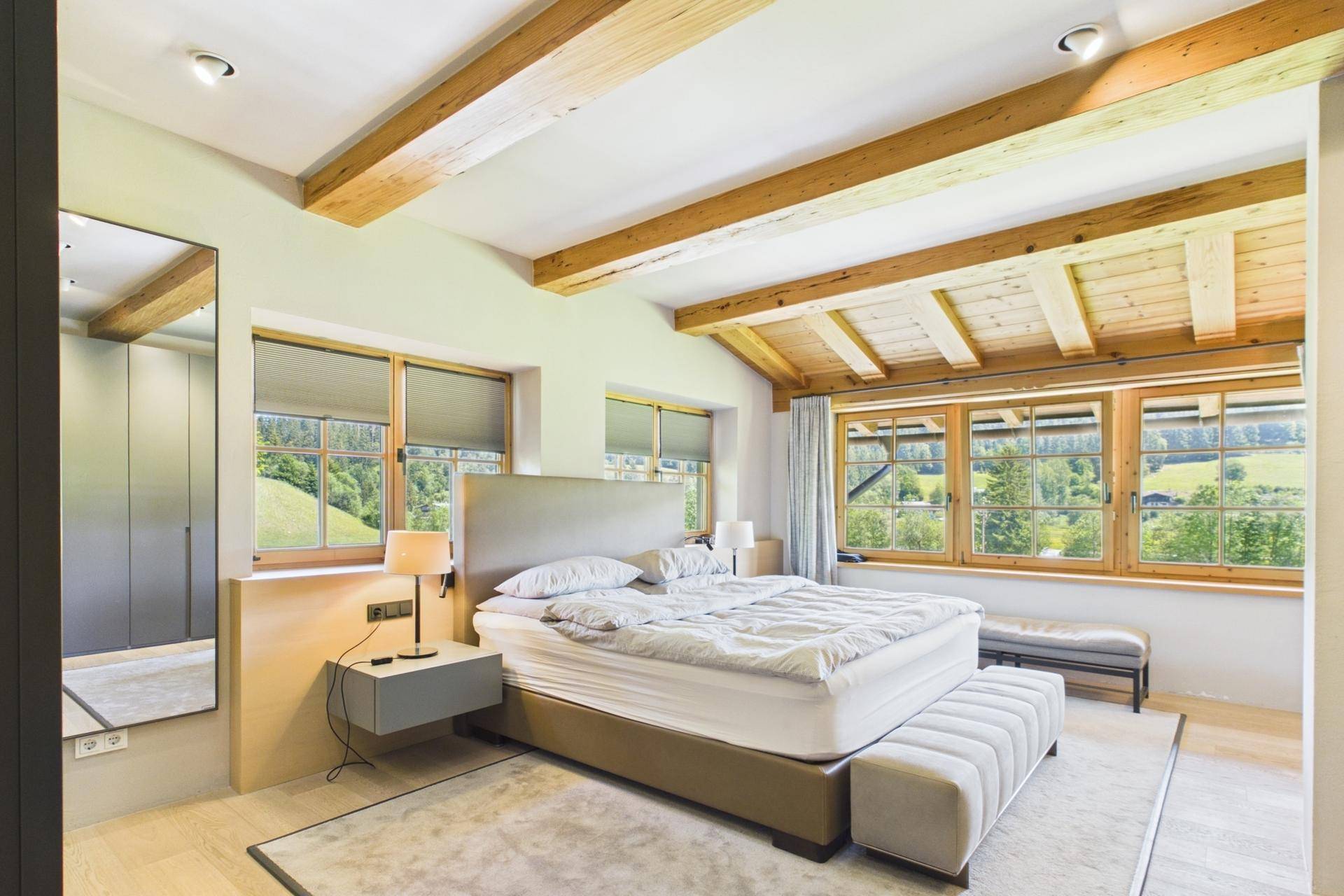 Geräumiges Schlafzimmer mit Holzbalkendecke, großen Fenstern und Bergblick.