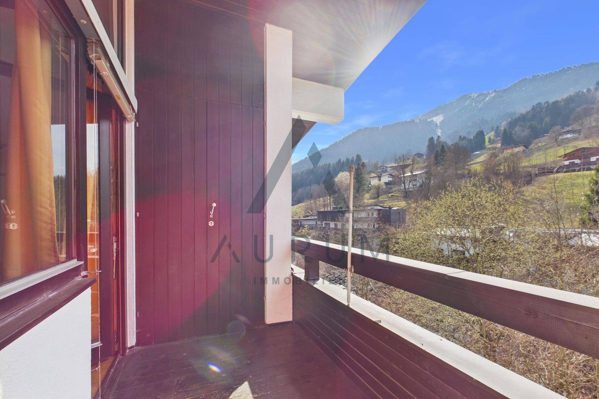 Sonniger Balkon mit Holzboden und Panoramablick auf die umliegende Bergwelt.