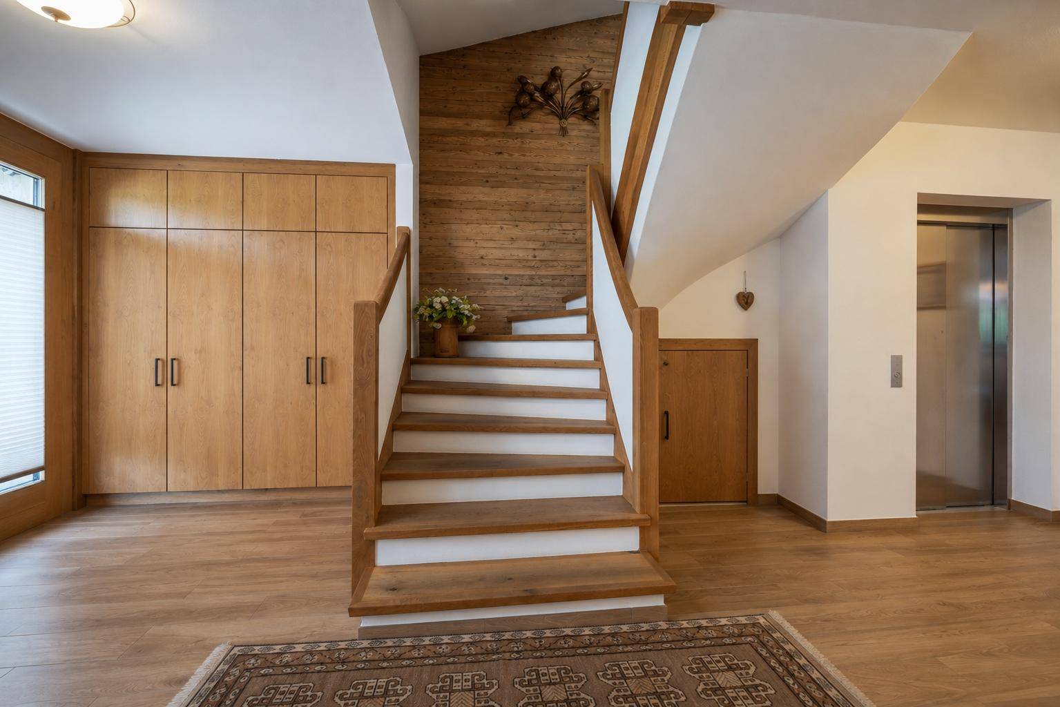 Heller Eingangsbereich mit Holztreppe, Einbauschränken und modernem Aufzug.
